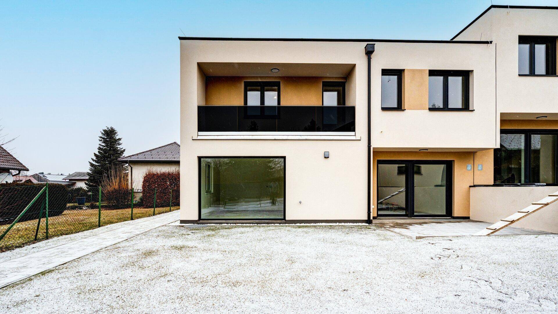 Ansicht eines modernen Reihenhauses mit großen Fenstern, Balkon und einer leicht verschneiten Rasenfläche.