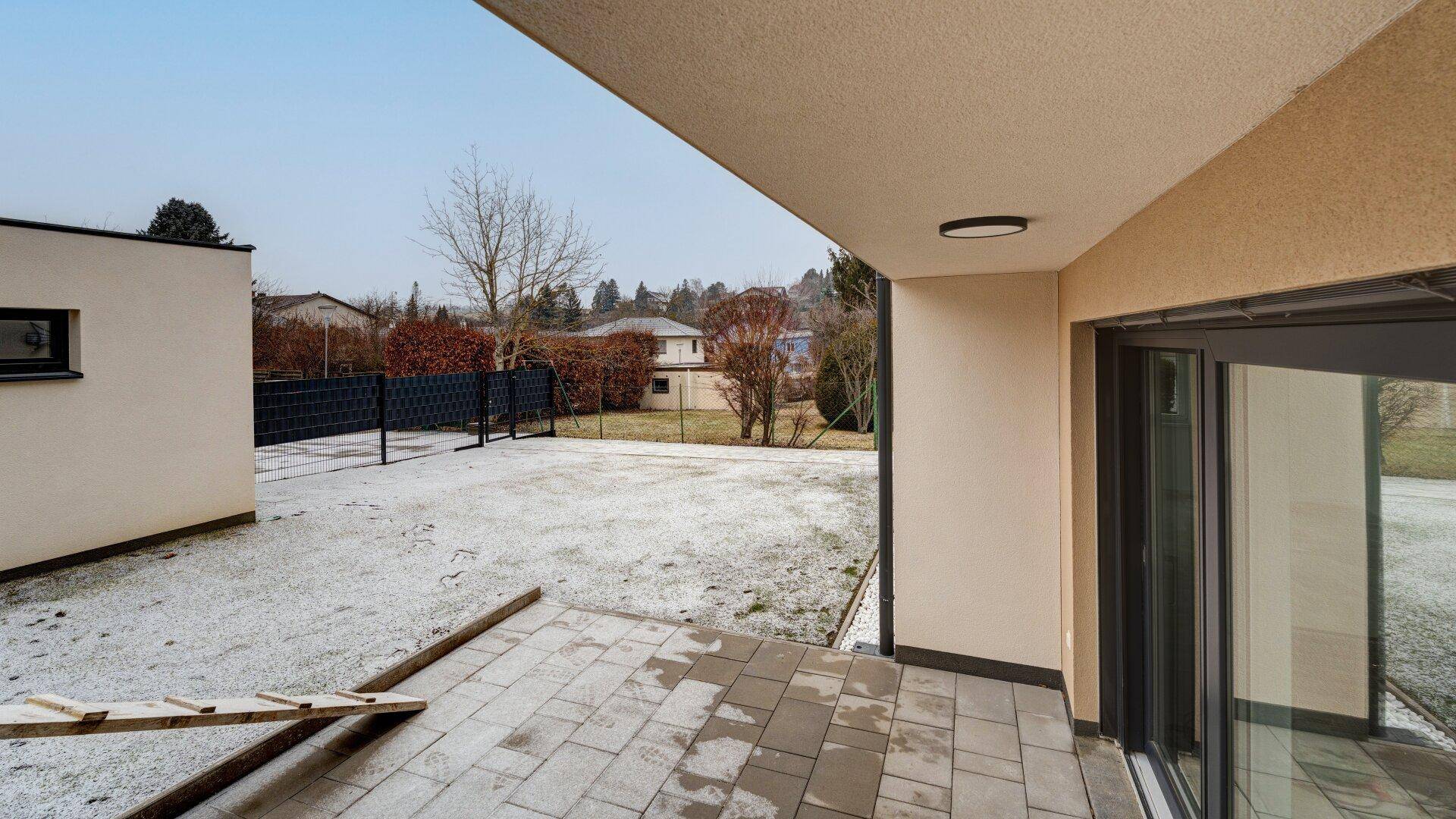 Eine gepflasterte Terrasse am Neubau mit Blick auf den Garten und die verschneite Umgebung.