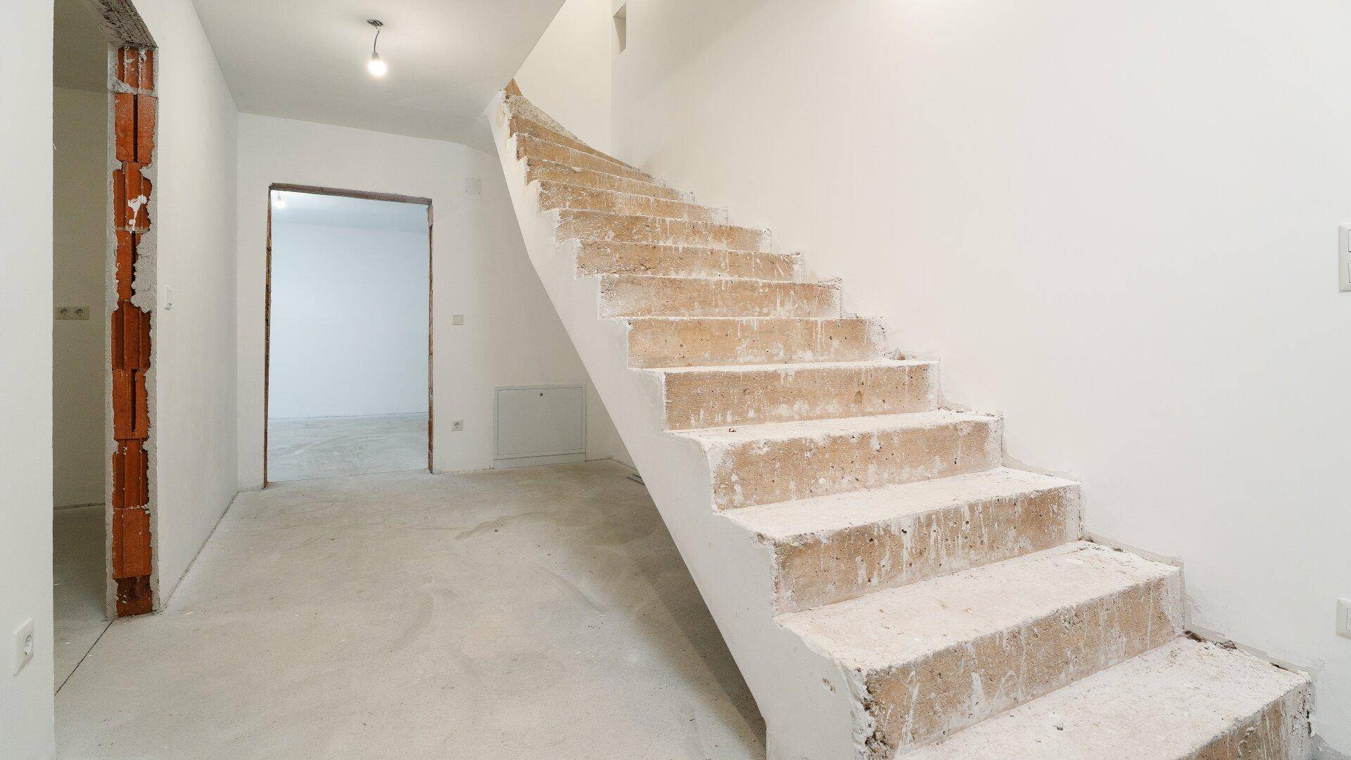 Treppenhaus im Rohbauzustand mit Betonstufen und weiß gestrichenen Wänden.