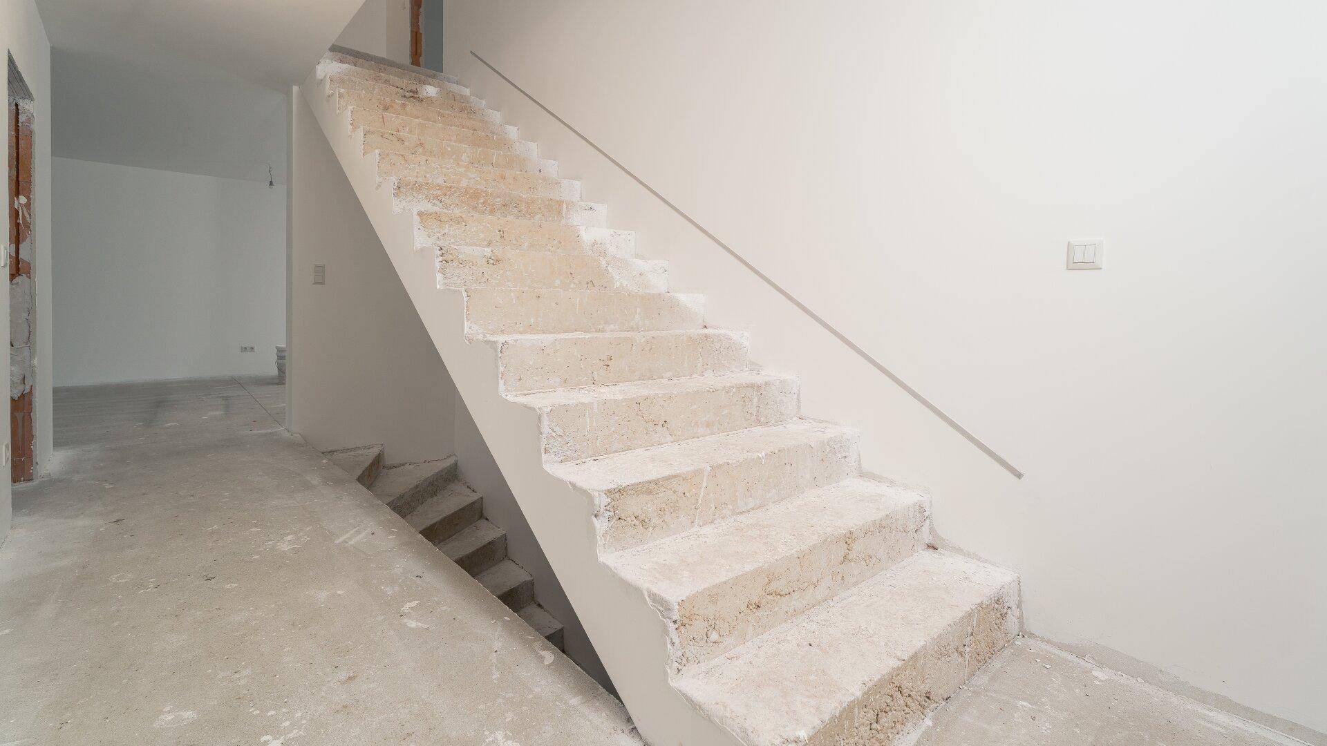 Treppenhaus im Rohbauzustand mit Betonstufen und weiß gestrichenen Wänden.