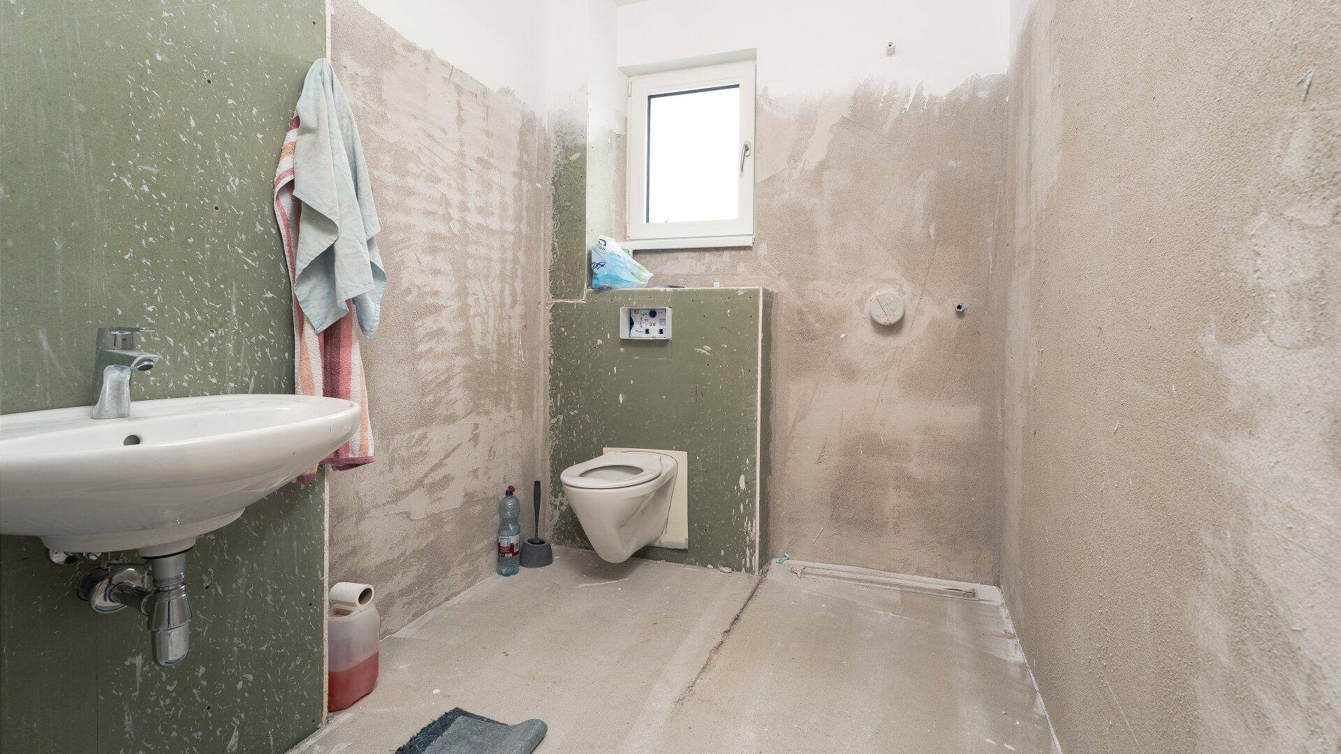 Badezimmer im Rohbauzustand mit Waschbecken, WC und Duschbereich, bereit für die Fertigstellung.