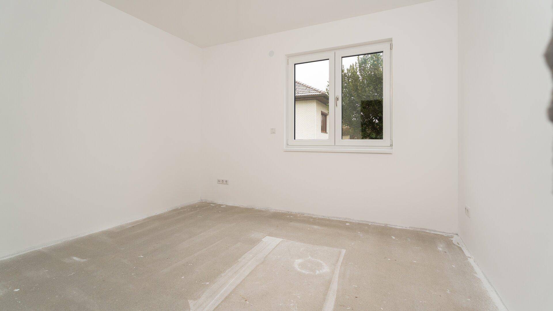 Raum im Rohbauzustand mit Fenster und weiß gestrichenen Wänden.