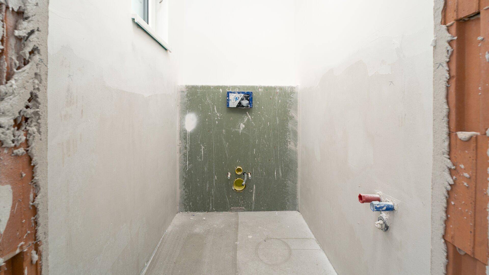 Kleiner Raum im Rohbauzustand mit sichtbaren Installationen für ein WC.