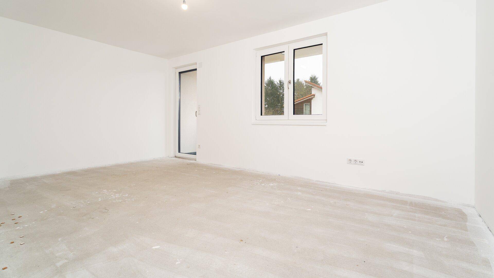 Großer Raum im Rohbauzustand mit Fenster und Zugang nach draußen.