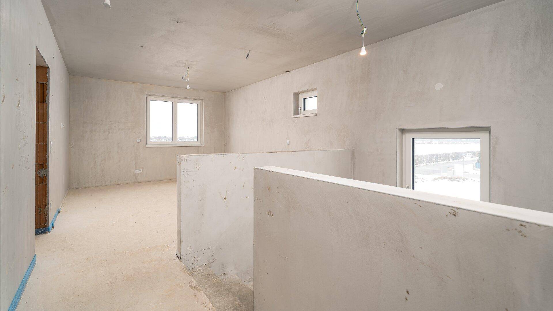 Unfertiger Flur im Obergeschoss mit Blick in einen weiteren Rohbau-Raum und Fenstern.