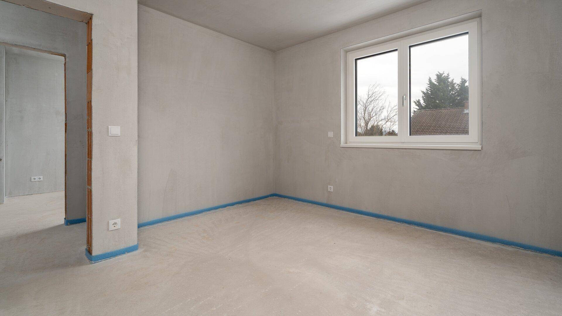 Unfertiger Raum im Rohbauzustand mit Fenster, bereit für die individuelle Gestaltung.
