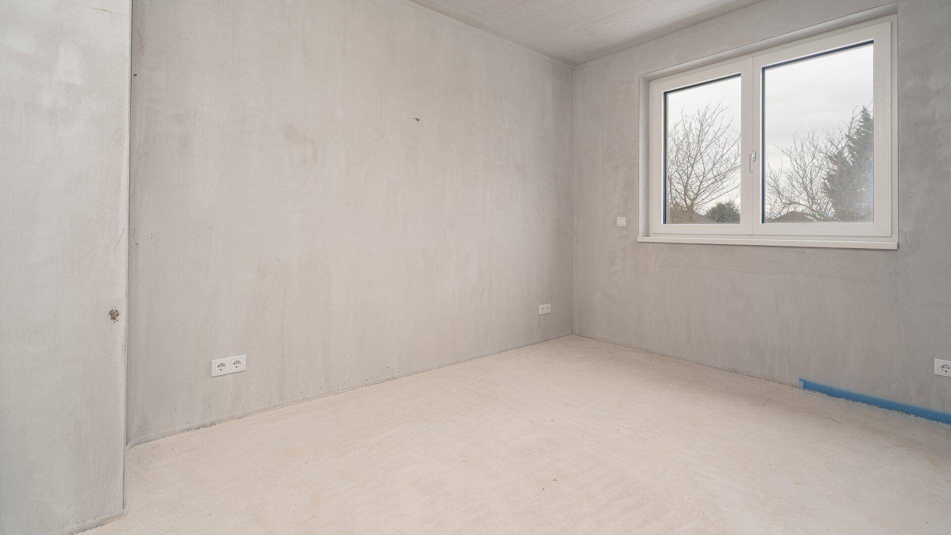 Unfertiger Raum im Rohbauzustand mit Fenster, bereit für die individuelle Gestaltung.
