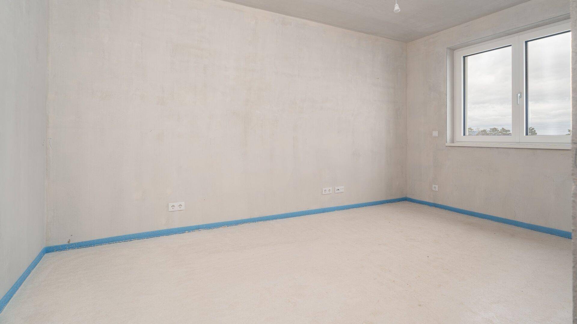 Unfertiges Schlafzimmer im Rohbauzustand mit Fenster, bereit für den Innenausbau.