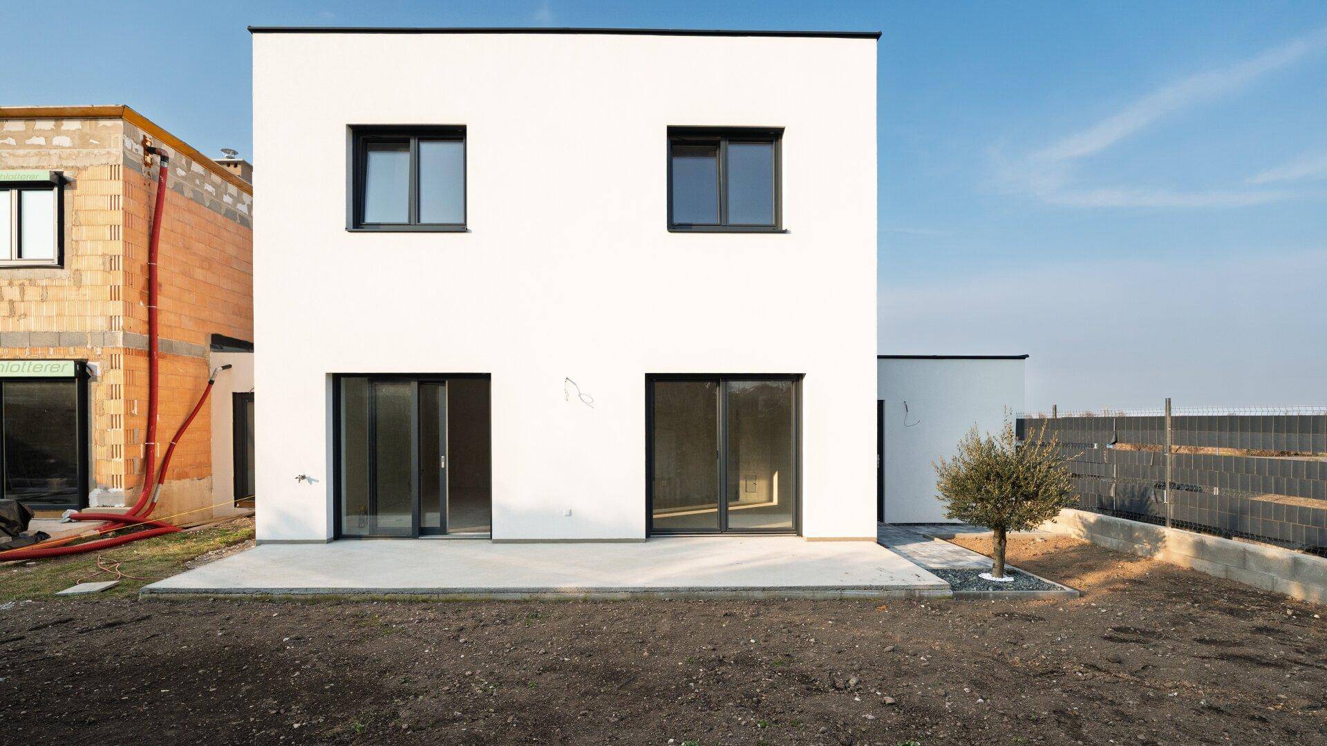 Rückansicht des modernen Neubaus mit weißer Fassade und einer Betonfläche, angrenzend an den Garten.