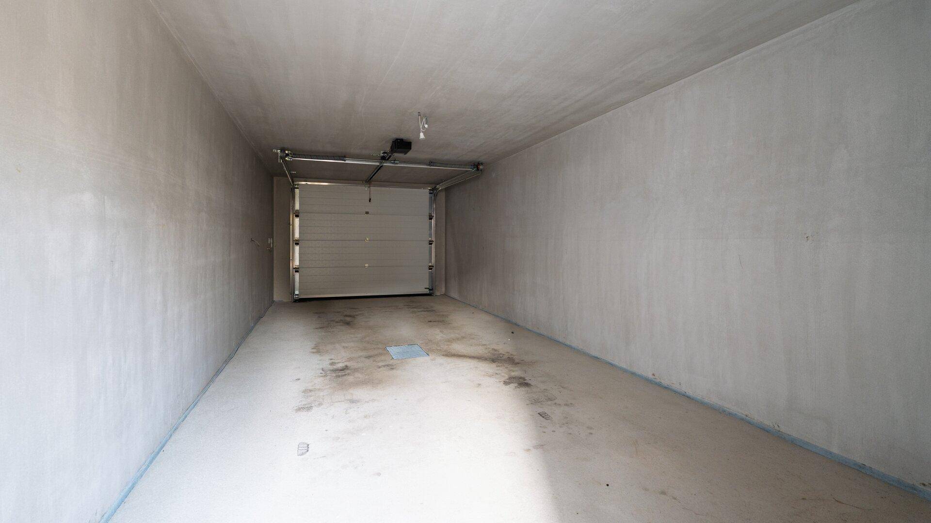 Unfertige Garage im Rohbauzustand mit Rolltor und Betonboden.
