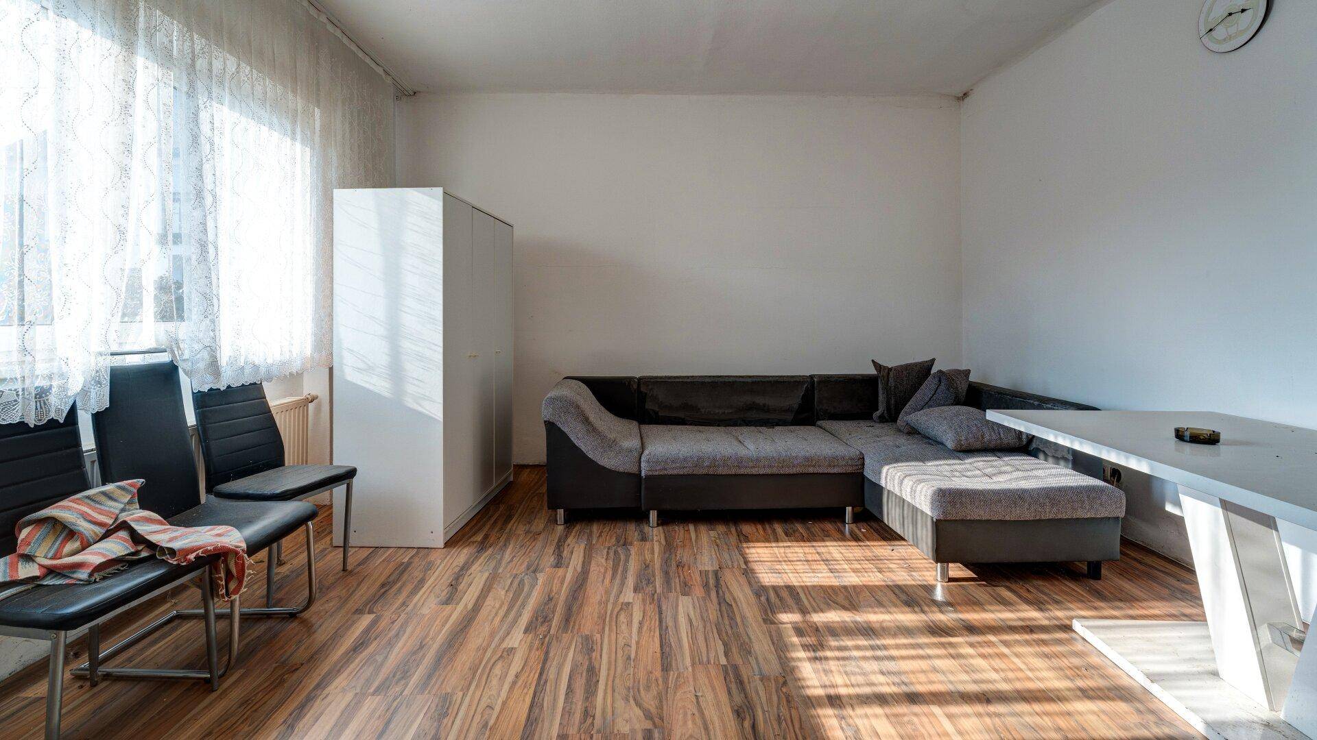 Wohnzimmer mit Laminatboden, Sofa und großem Fenster für viel Tageslicht.