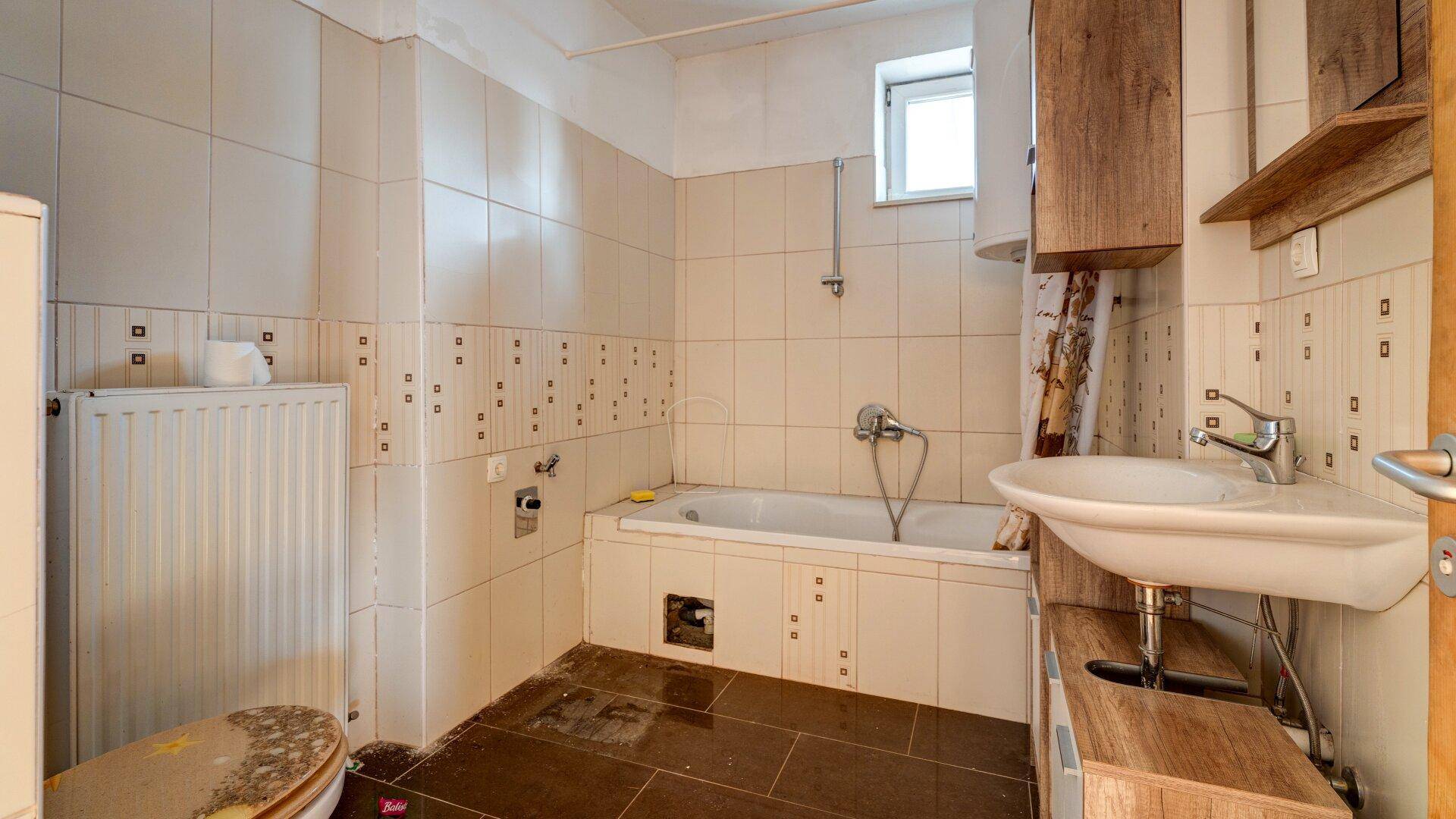 Badezimmer mit Badewanne, Waschbecken und Fenster, gefliest in Beige und Braun.