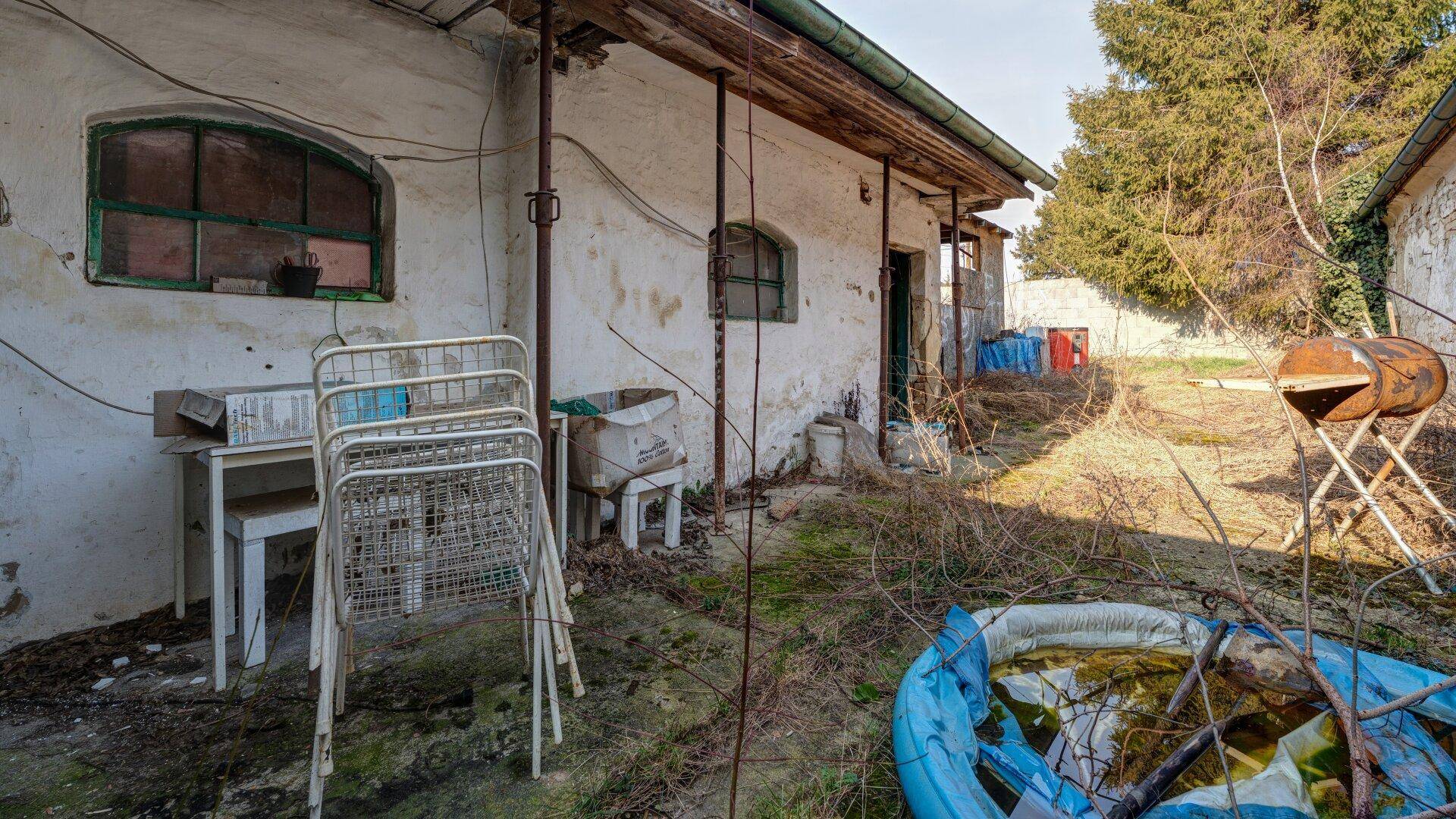 Ungepflegter Gartenbereich hinter dem Haus mit alten Möbeln und Pflanzen.