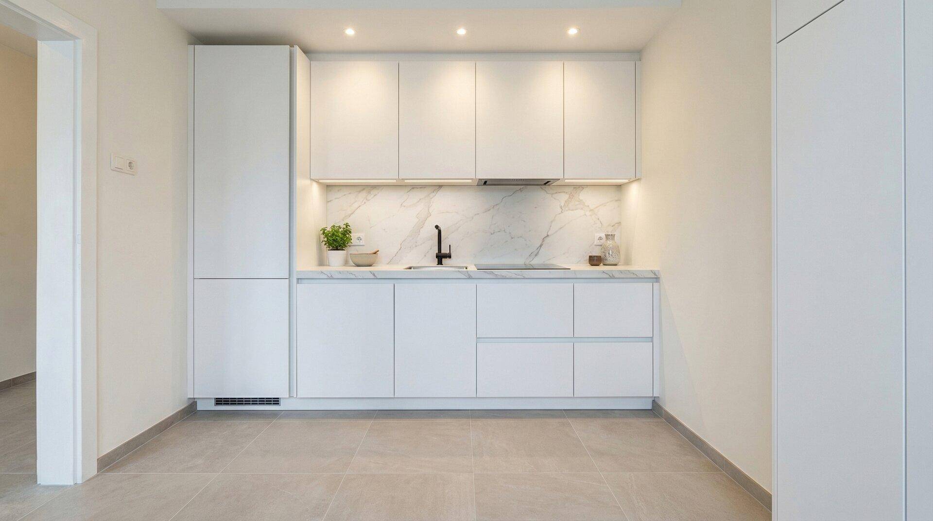 Moderne, helle Küche mit weißen Schränken, Marmor-Optik-Rückwand und integrierten Geräten.