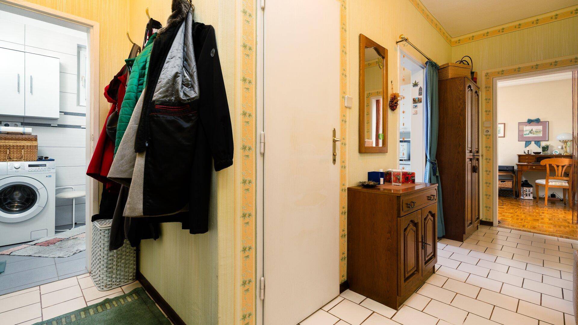 Flur mit Fliesenboden, Garderobe und Zugang zu einem Raum mit Waschmaschine.