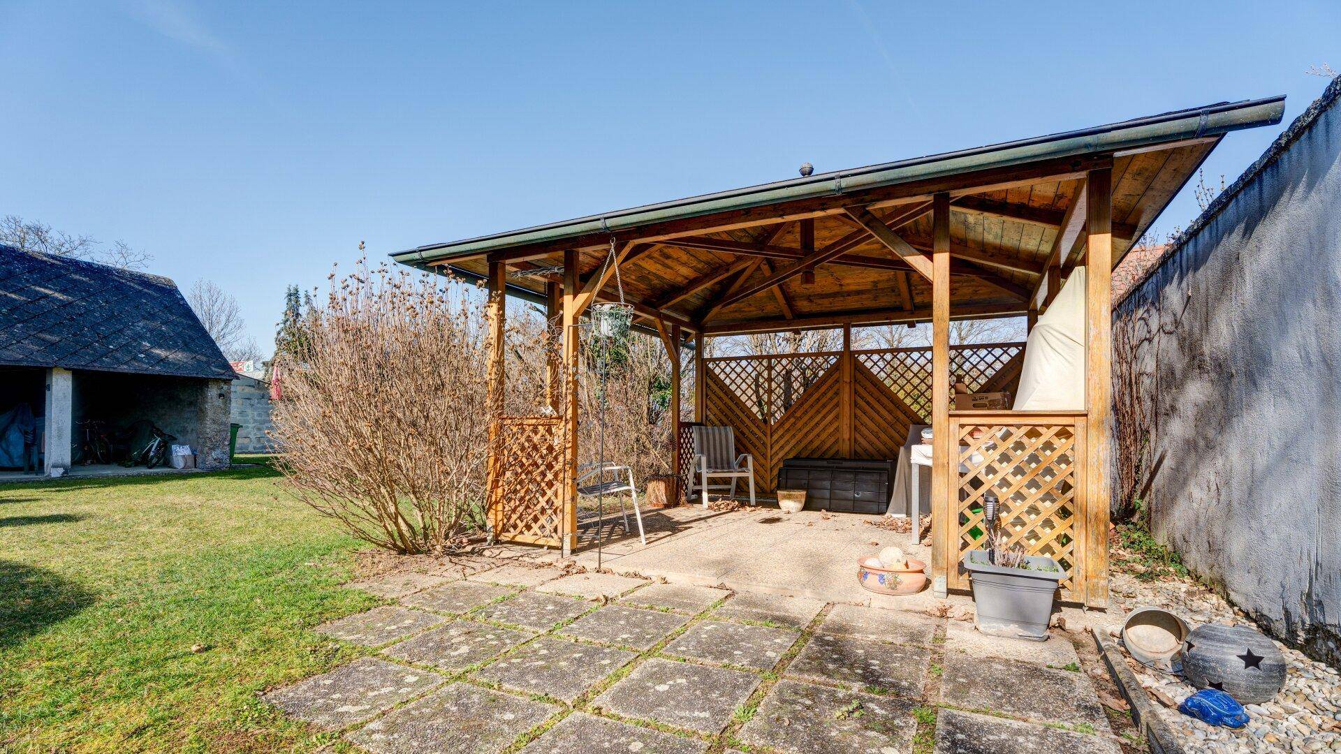 Gemütlicher Gartenpavillon auf einer gepflasterten Terrasse, umgeben von Grünflächen.