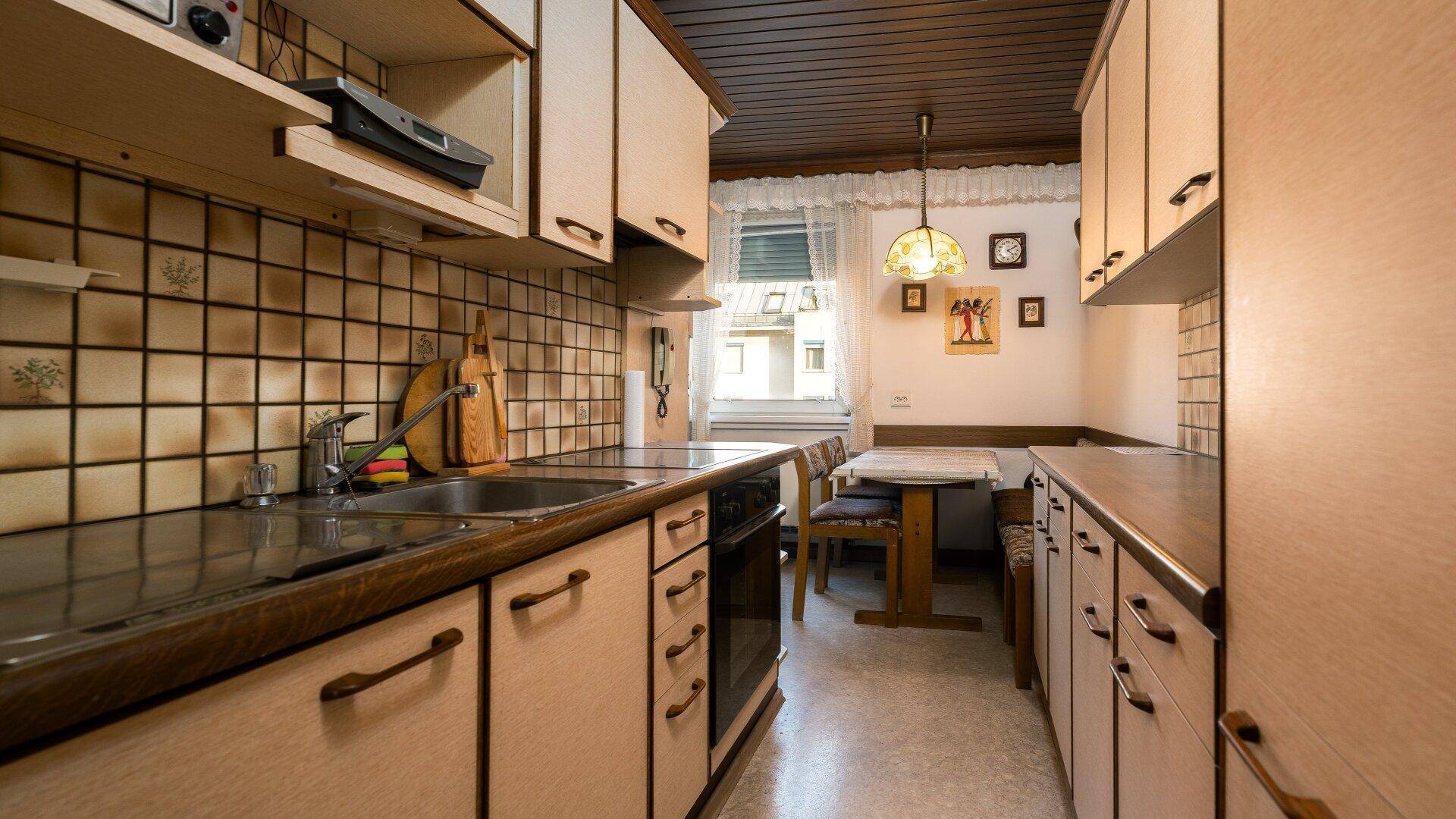 Funktionale Küche mit Holzschränken, gefliestem Spritzschutz und einem kleinen Essbereich am Fenster.