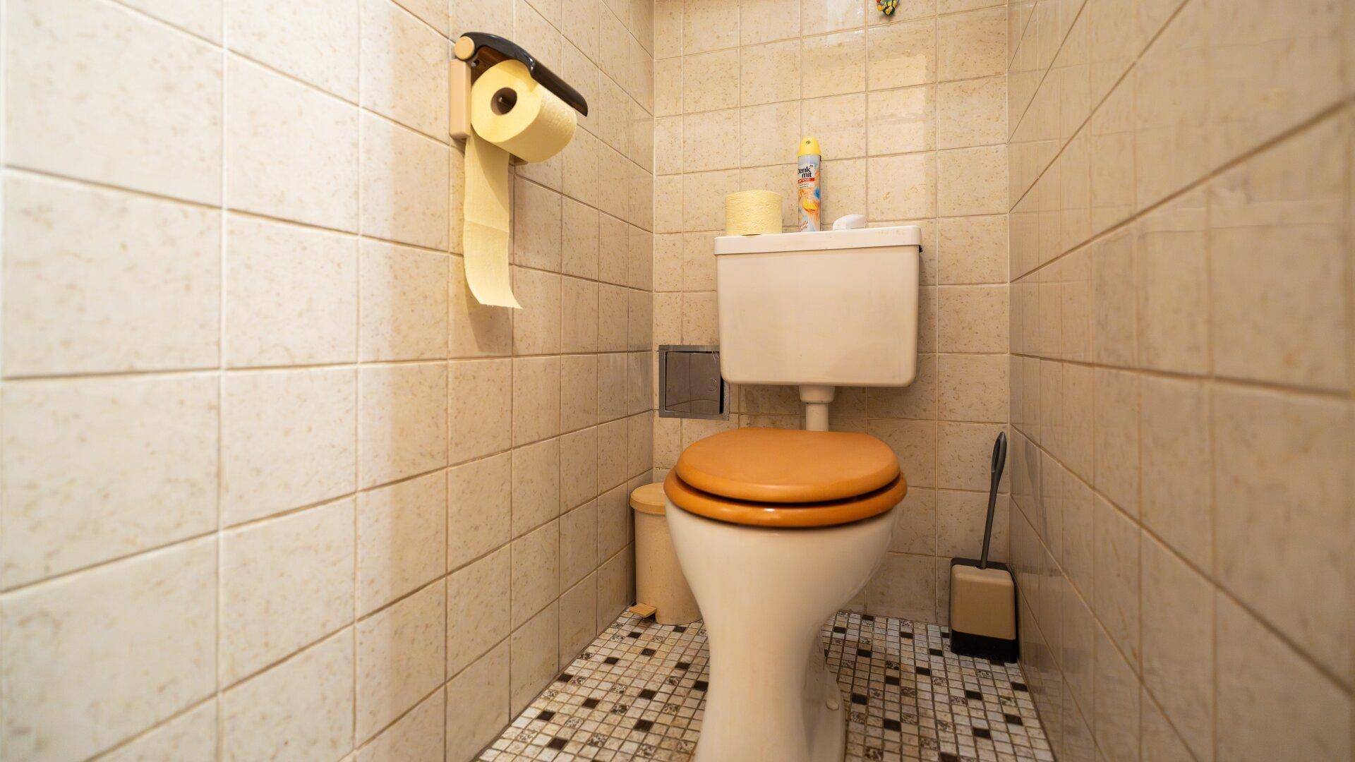 Kleines WC mit beigen Fliesen, Toilette und einem kleinen Mülleimer, funktional und einfach gehalten.