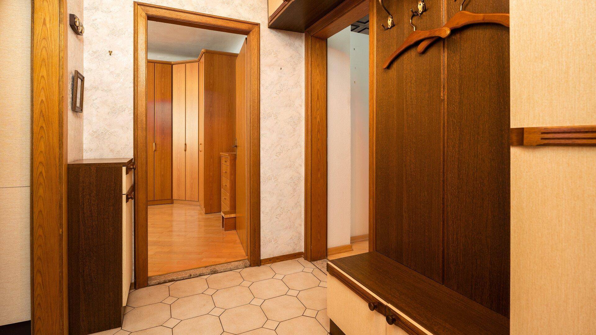 Flur mit hellen Fliesen, dunkler Holzgarderobe und Zugang zu weiteren Räumen der Wohnung.