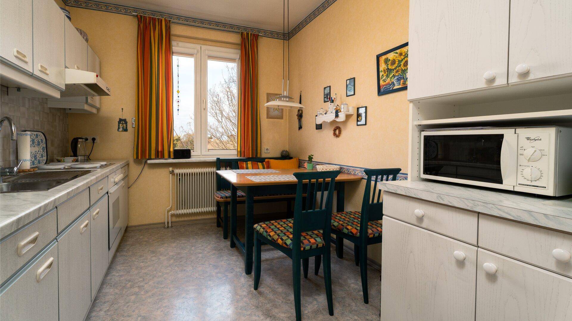 Funktionale Küche mit Essbereich, Mikrowelle und hellen Schränken, gut beleuchtet durch ein Fenster.