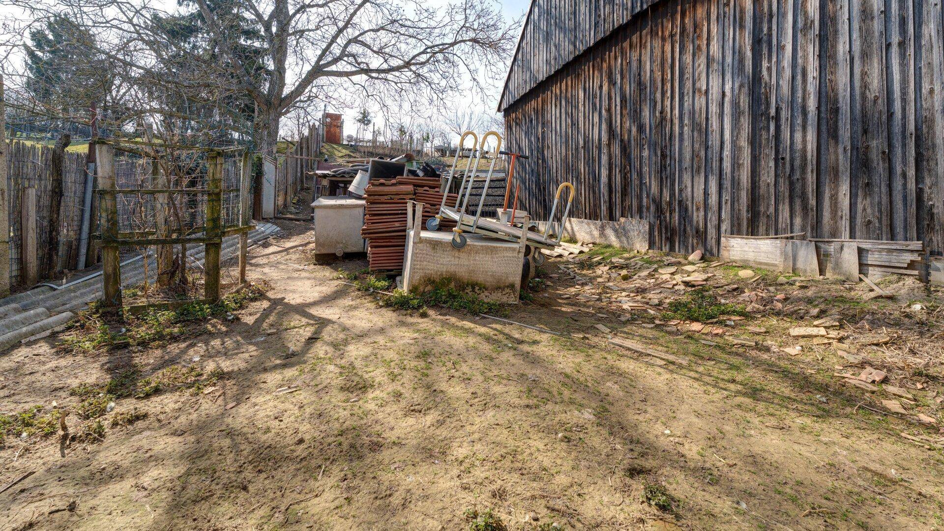 Ungepflegter Gartenbereich mit altem Holzschuppen und verschiedenen Materialien.