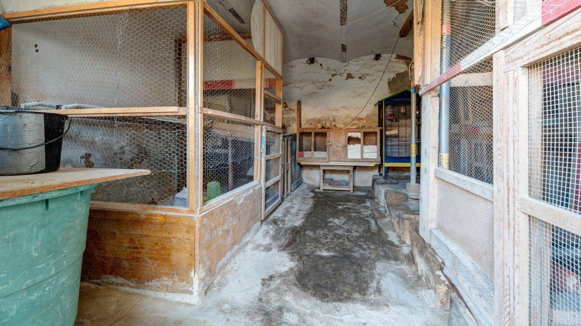 Alter Scheunenbereich mit Holz- und Drahtgeflecht-Gehegen und unebenem Boden.