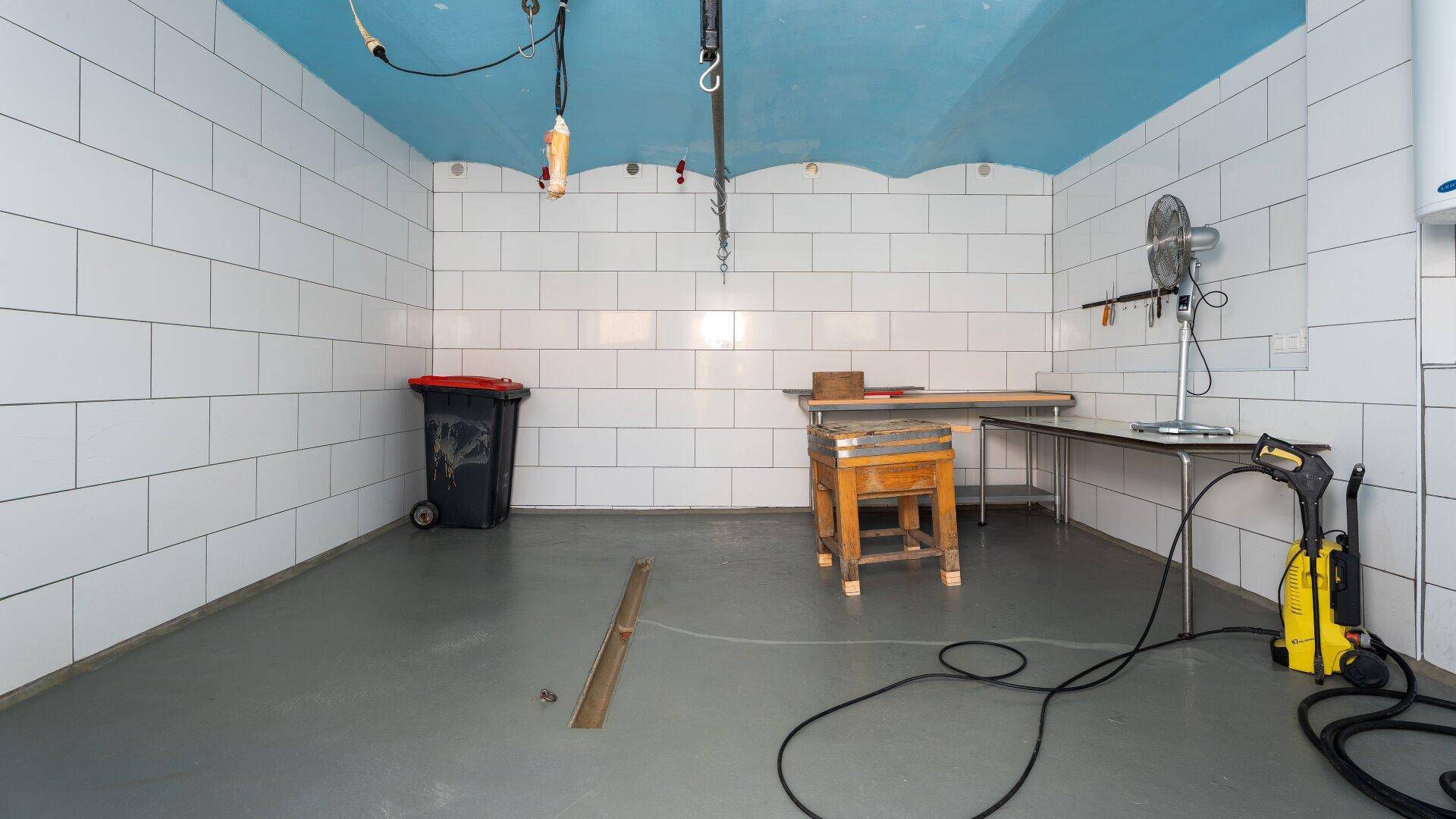Gefliester Raum mit blauer Decke, Arbeitstischen und Reinigungsgeräten.