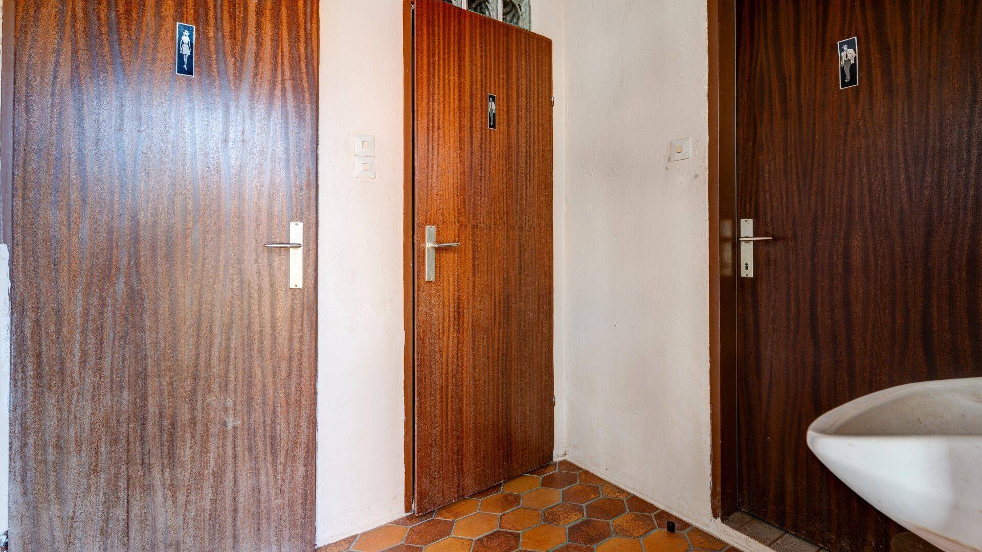 Bereich mit mehreren Holztüren zu Toiletten und einem kleinen Waschbecken.