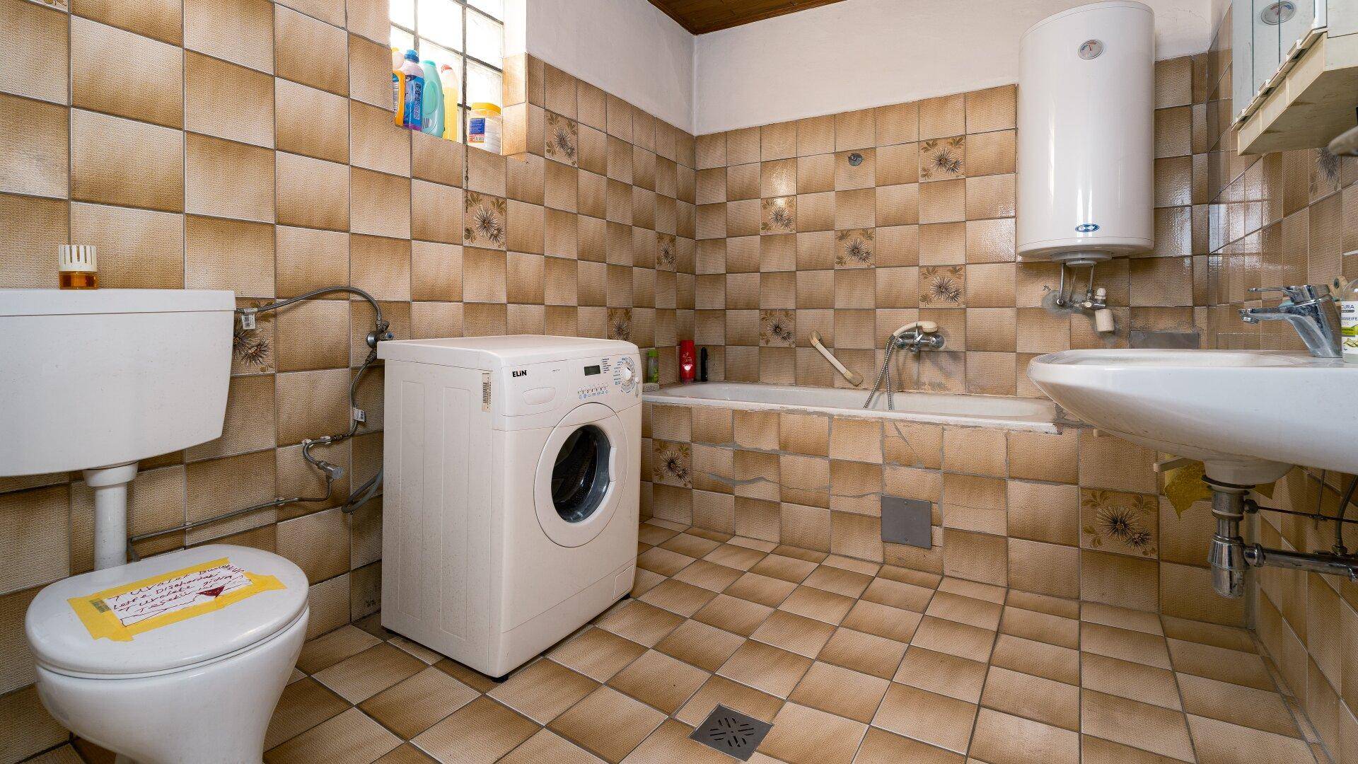 Badezimmer mit braunen Fliesen, Badewanne, Toilette und Waschmaschine.