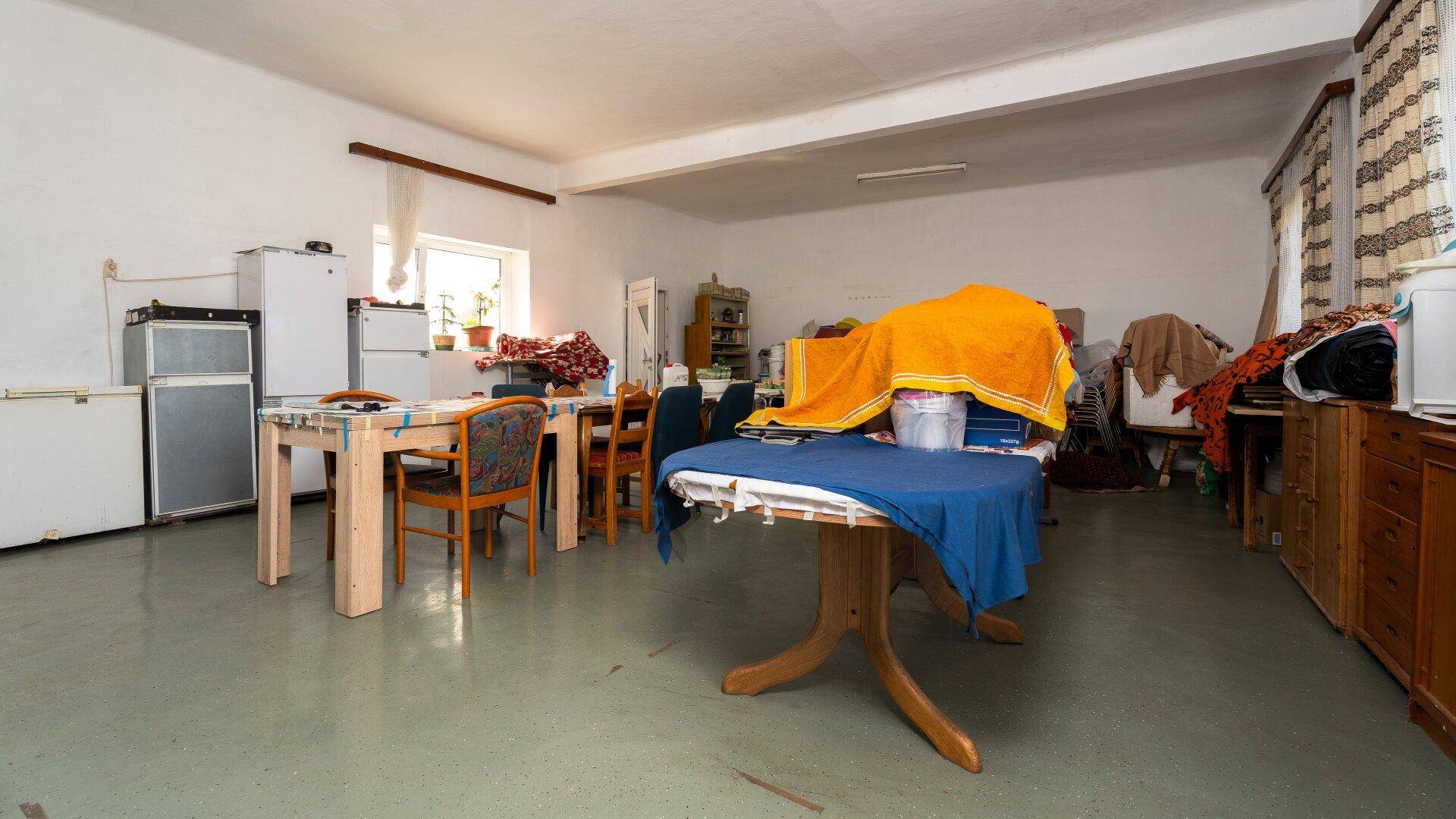 Großer Mehrzweckraum mit Tischen, Kühlschränken und verschiedenen Haushaltsgegenständen.