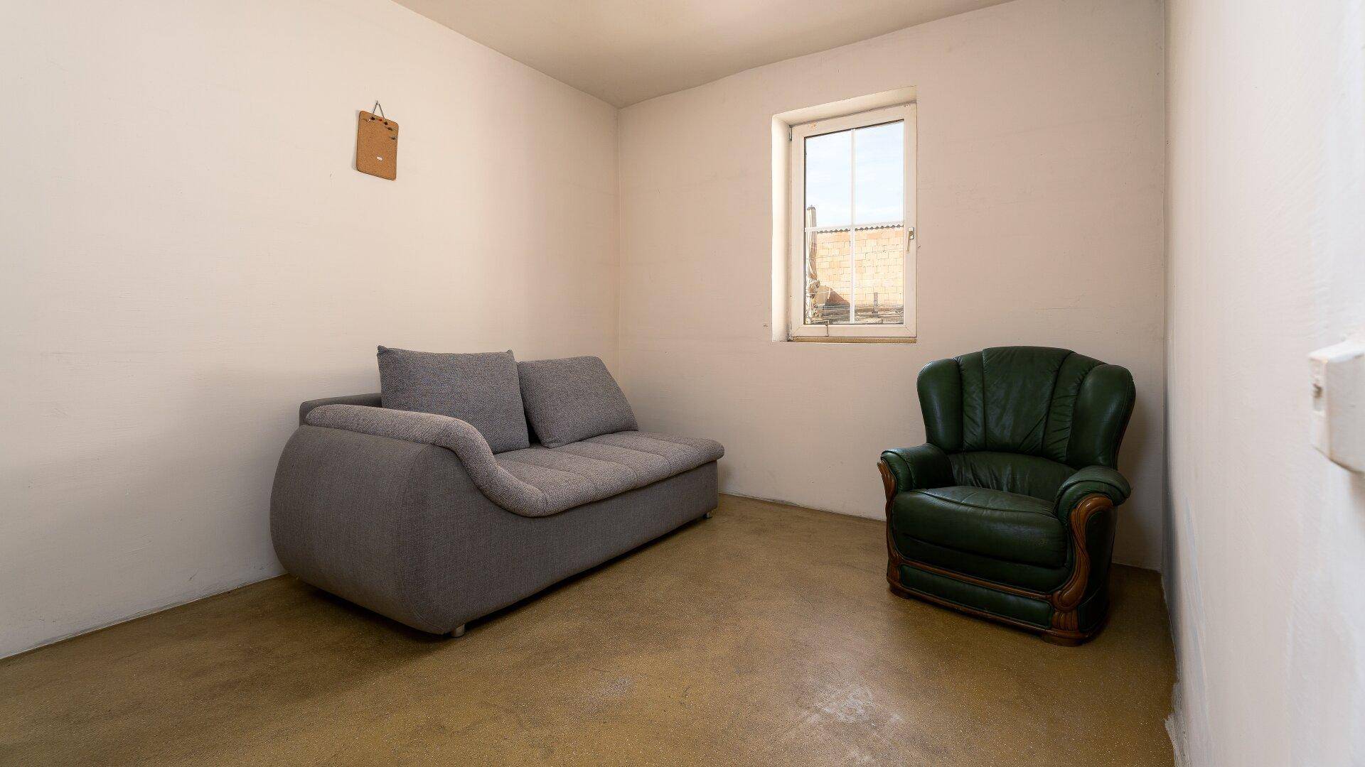 Einfaches Wohnzimmer mit einem grauen Sofa und einem grünen Ledersessel.