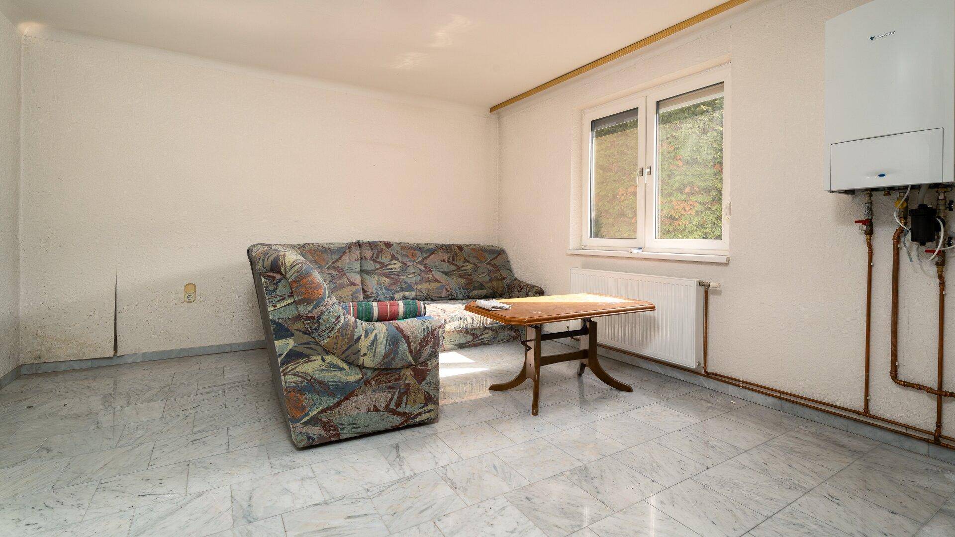 Gemütlicher Wohnbereich mit Sofa, Fliesenboden und Heizungsanlage an der Wand.