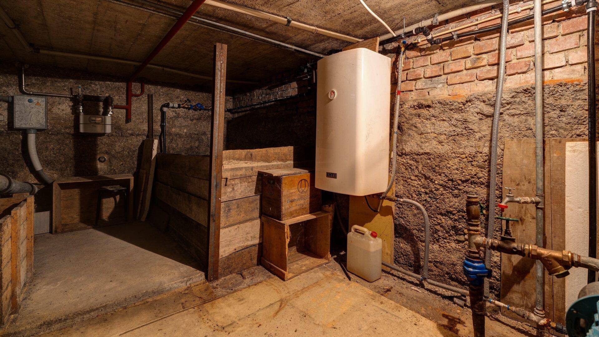 Kellerraum mit freiliegenden Rohren, Ziegelwänden und einem Warmwasserbereiter.