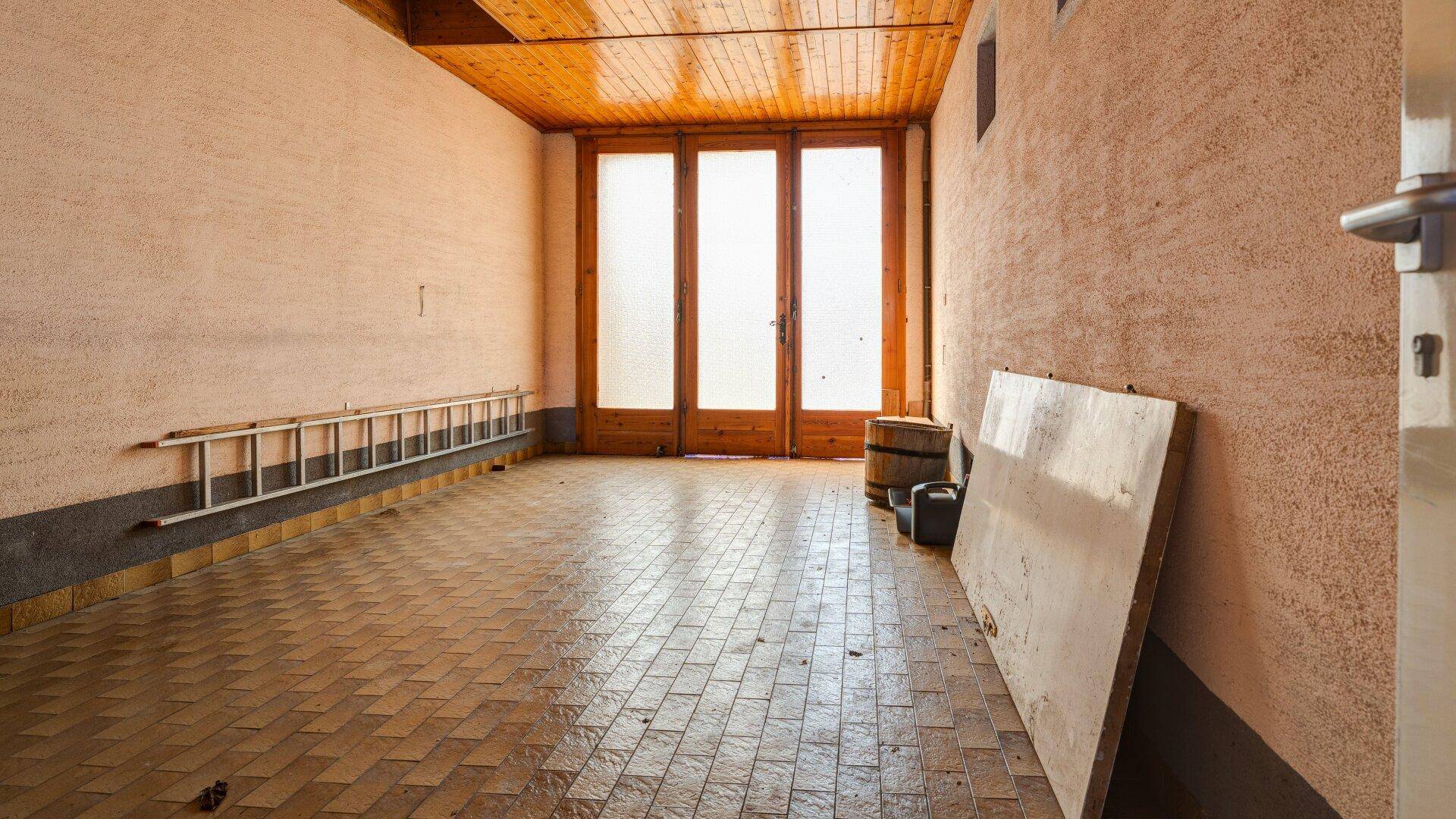 Geräumiger Abstellraum mit Fliesenboden und großen Fenstertüren, ideal für Lagerung.
