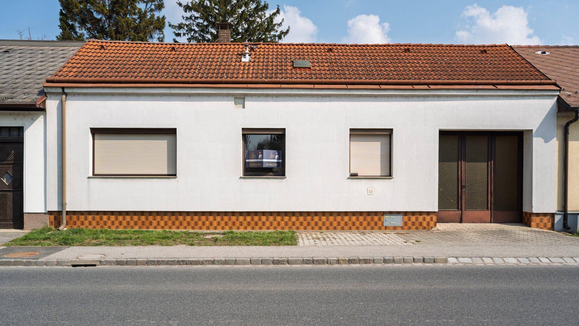Vorderansicht des Hauses mit weißer Fassade, Rollläden und einem roten Satteldach.