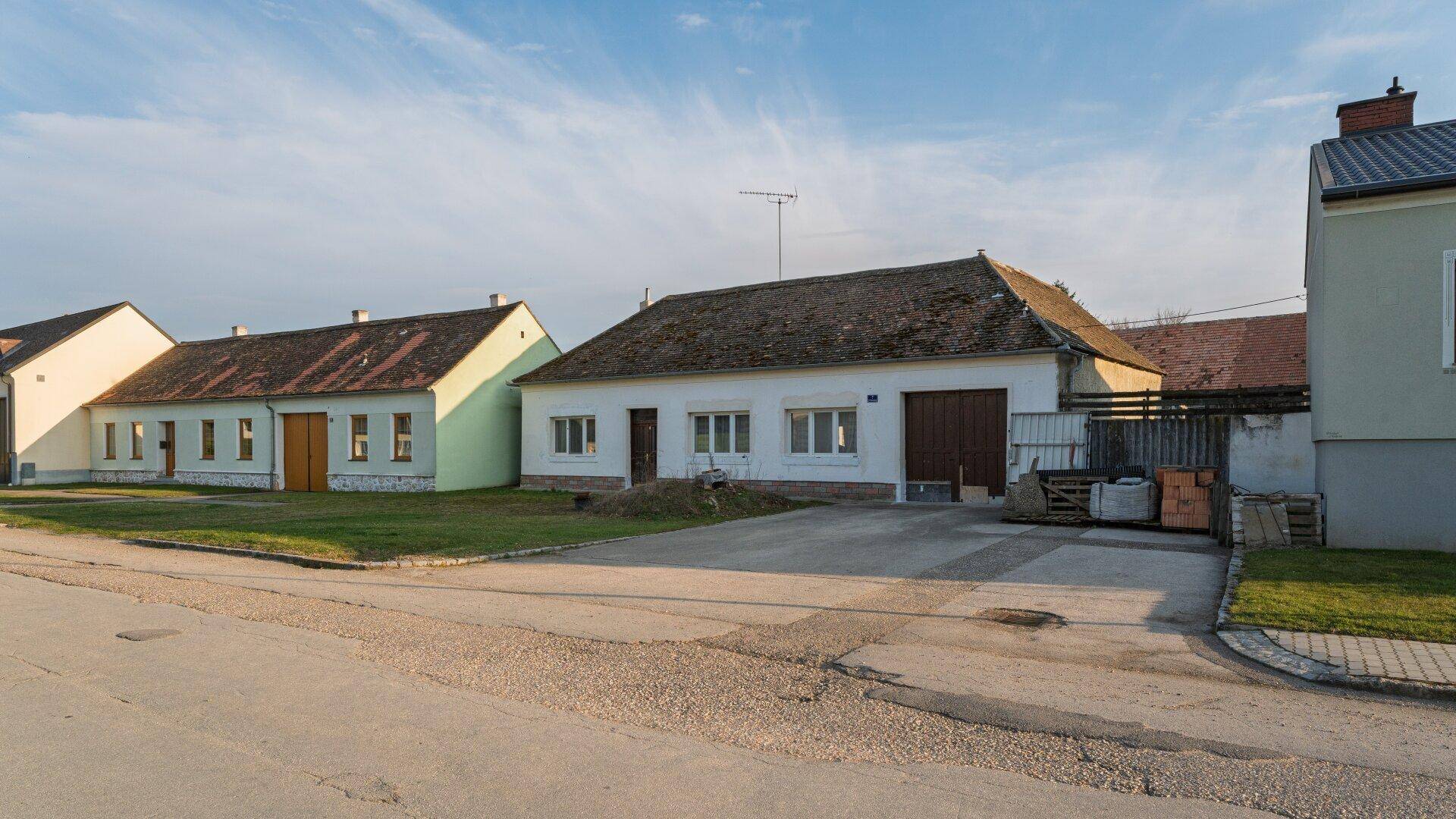 Ansicht eines ländlichen Hauses mit Vorgarten und angrenzender Straße unter blauem Himmel.