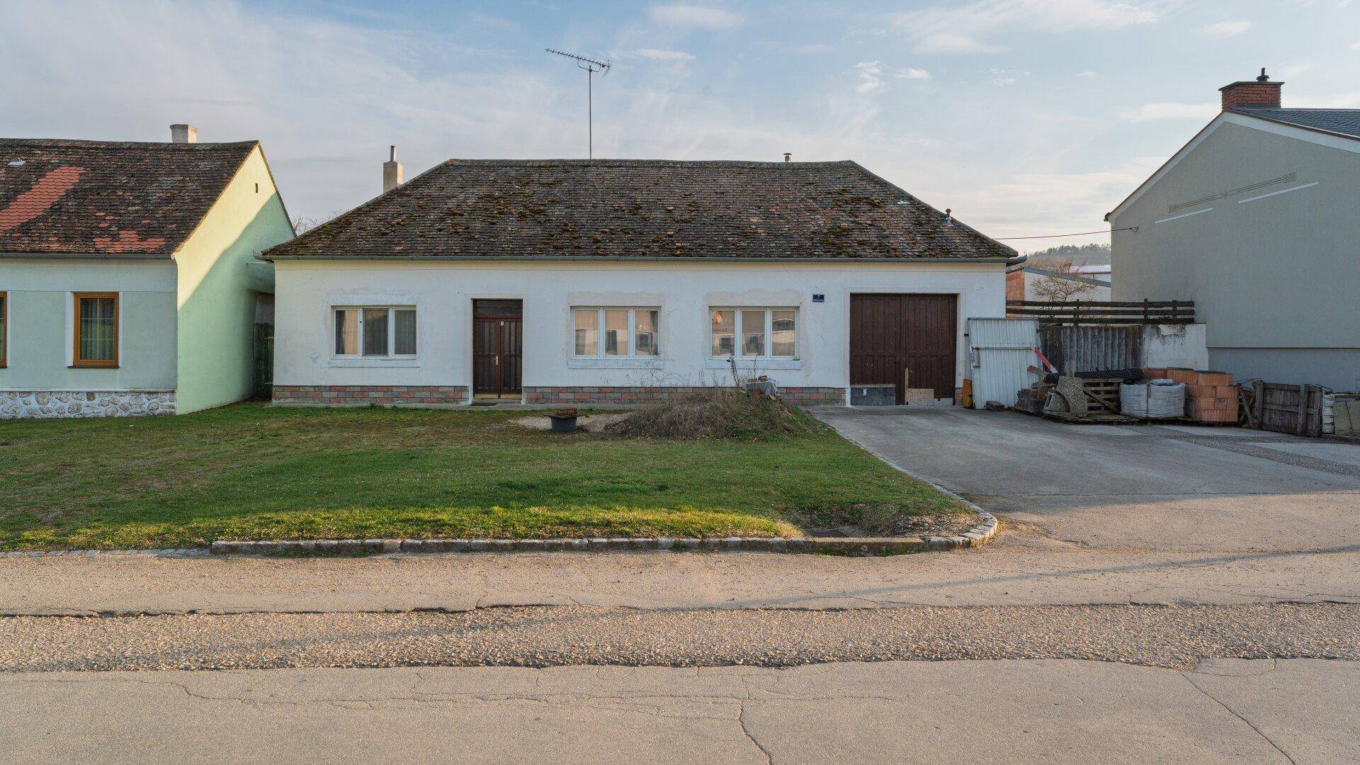Vorderansicht eines einfachen Einfamilienhauses mit Garage und grünem Vorgarten.