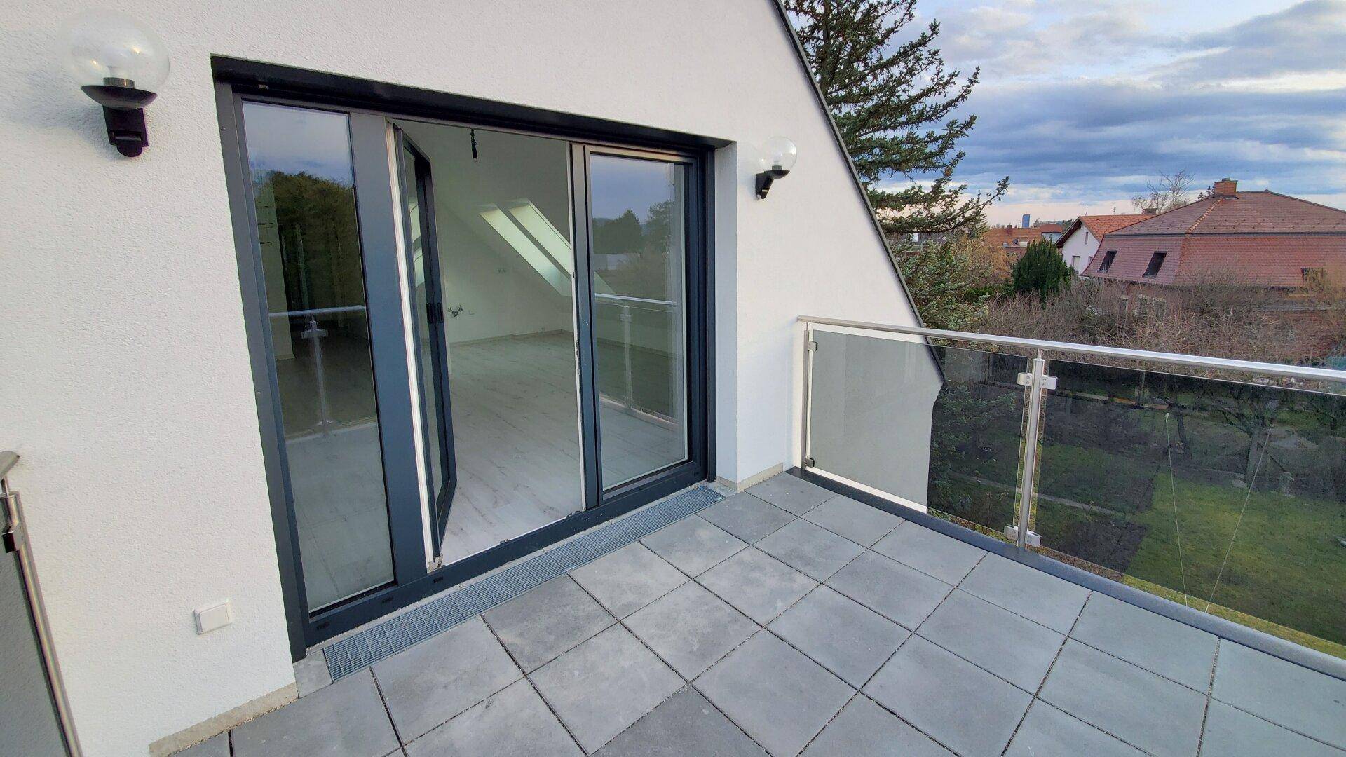 Geräumiger Balkon mit Fliesenboden und Glasgeländer, Zugang zum Innenraum.
