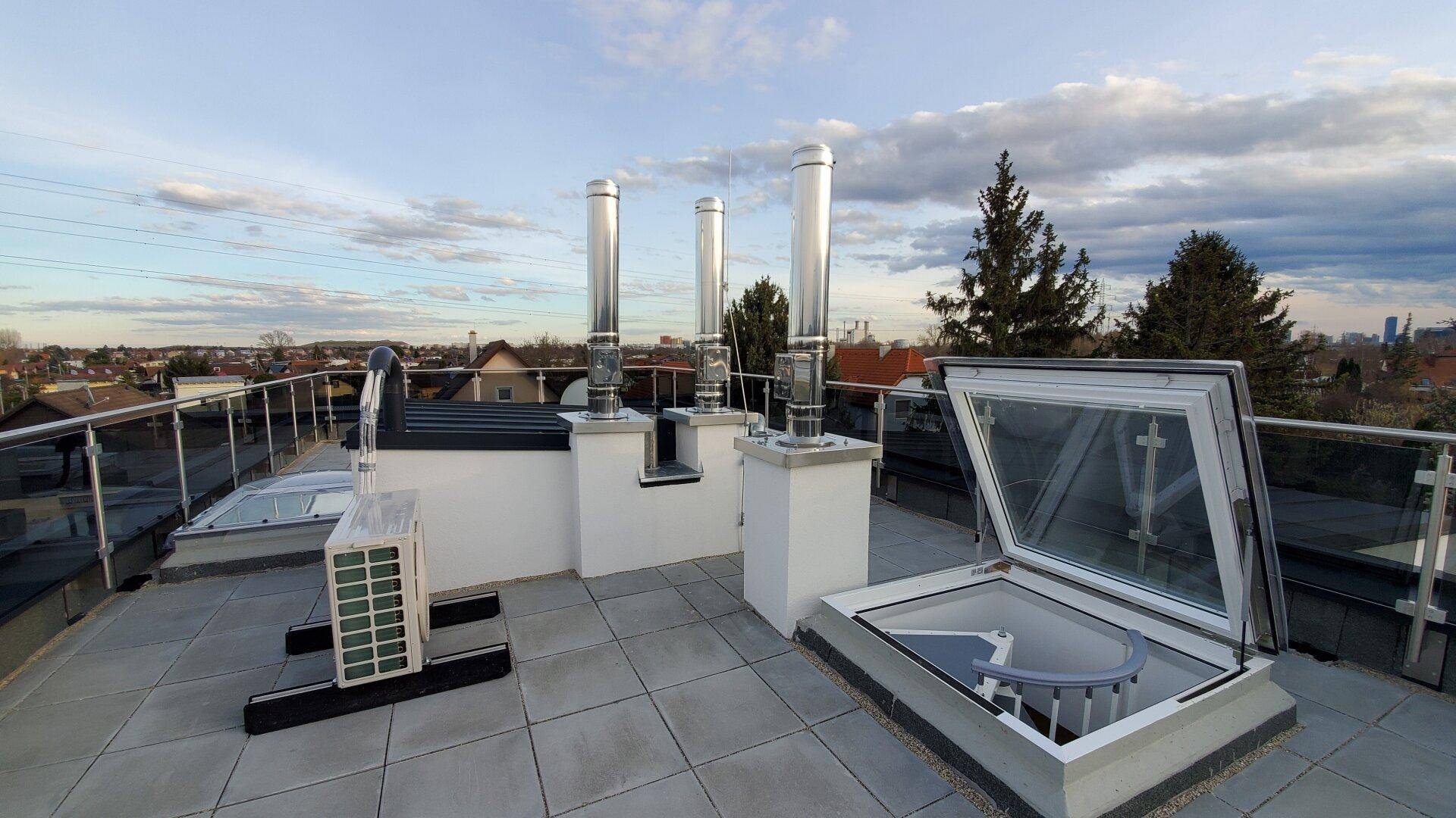 Dachterrasse mit Fliesenboden, Glasgeländer und Blick über die Umgebung bei Sonnenuntergang.