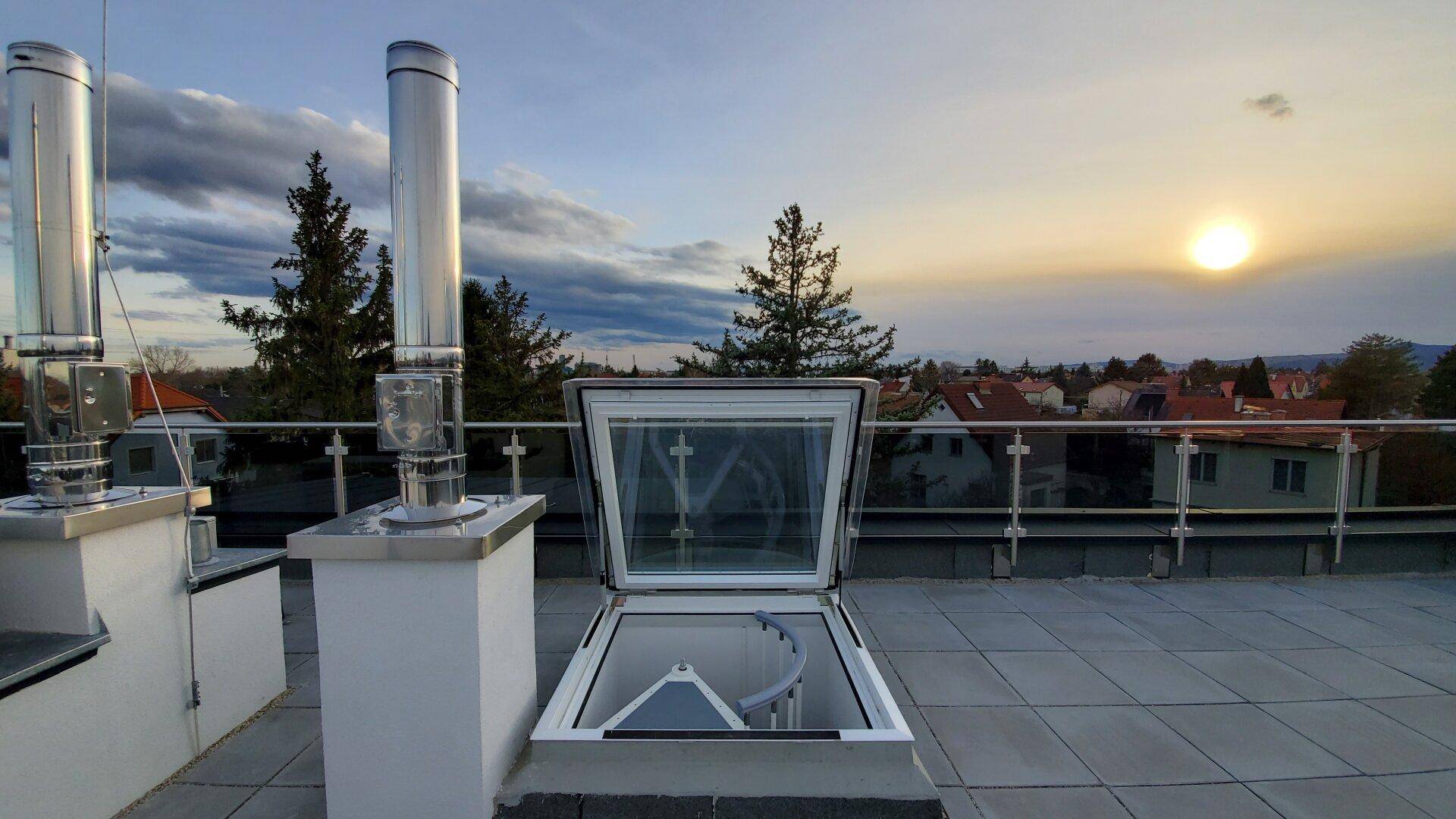Dachterrasse mit Zugang über Dachluke und Blick auf die Umgebung bei Sonnenuntergang.