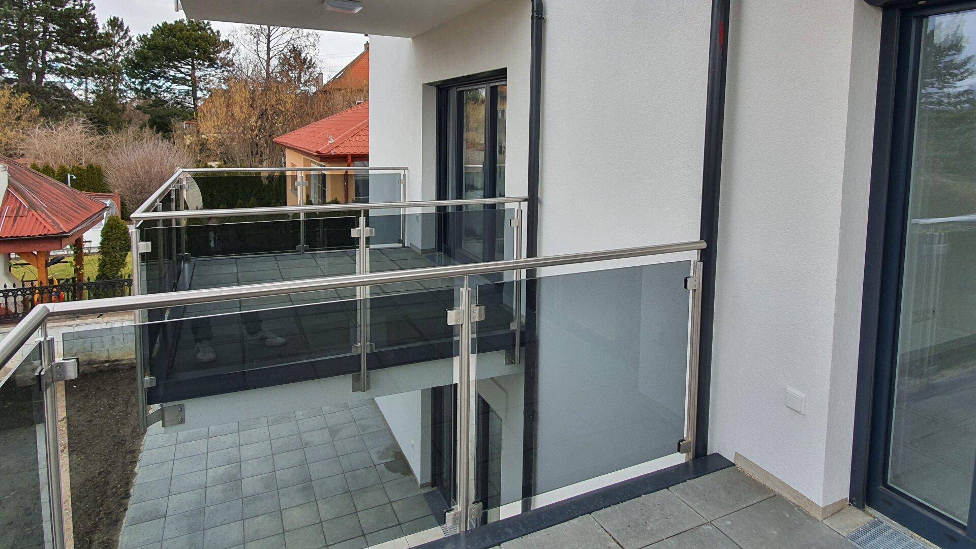 Zwei übereinanderliegende Balkone mit Glasgeländer und Fliesenboden an der Gebäudefassade.