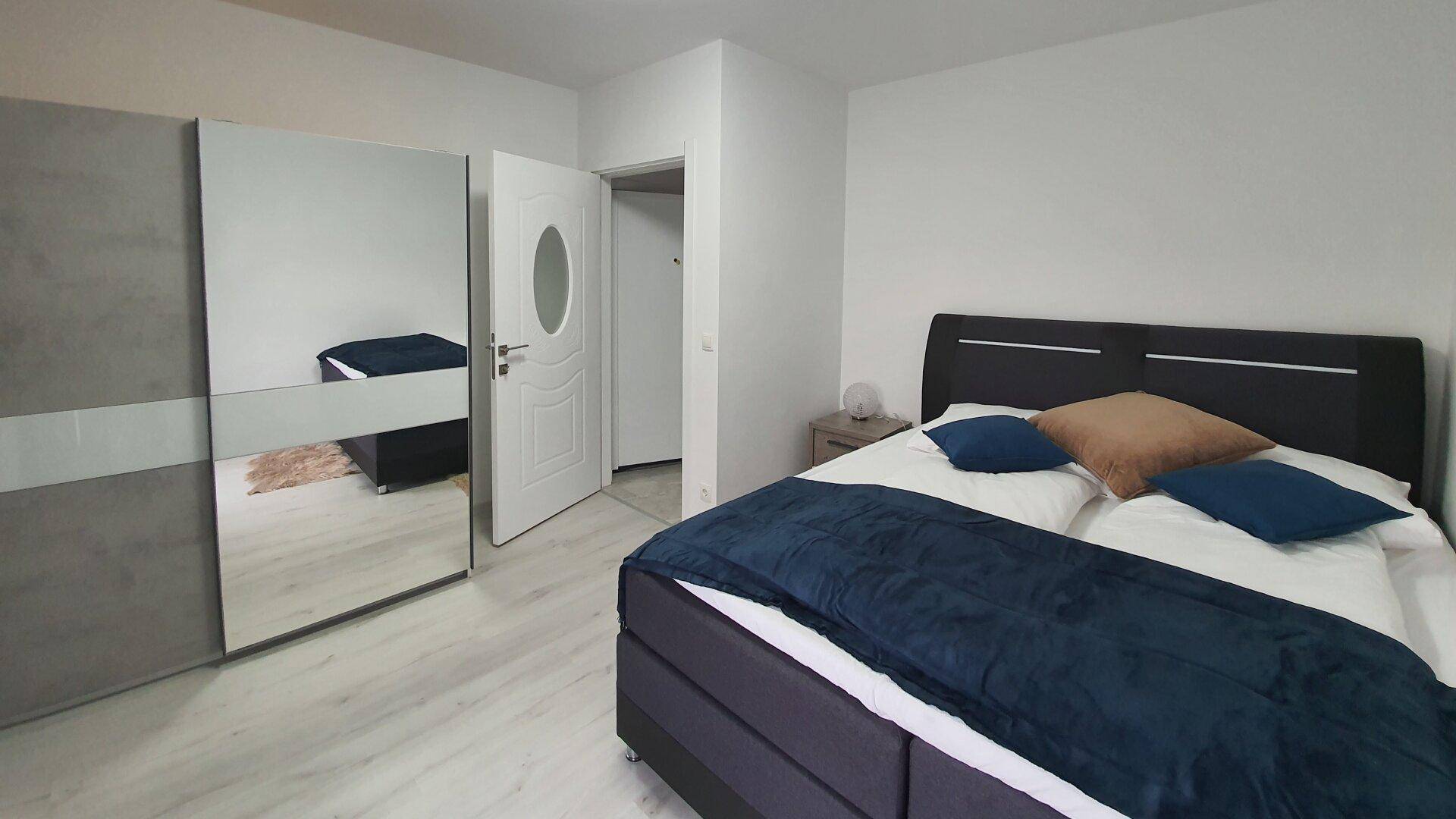 Helles Schlafzimmer mit Doppelbett, Spiegelschrank und hellem Laminatboden.