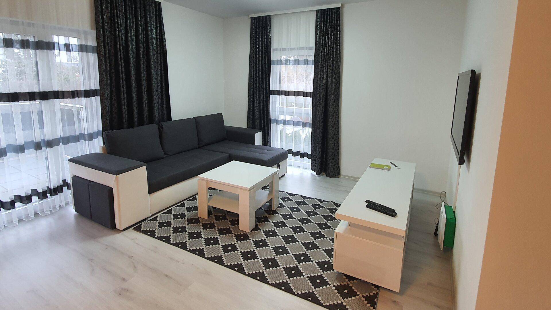 Gemütliches Wohnzimmer mit Ecksofa, Couchtisch und dunklen Vorhängen, helles Laminat.