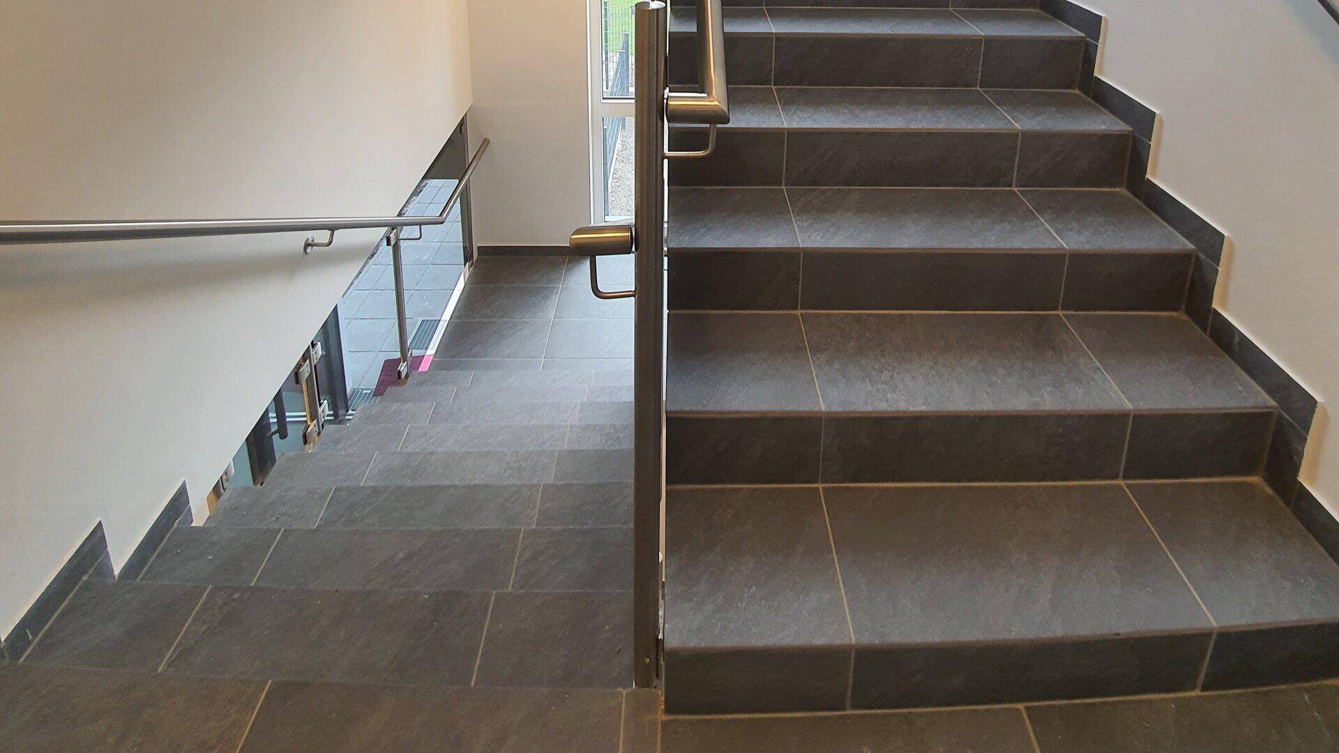 Modernes Treppenhaus mit dunklen Fliesenstufen und Edelstahlgeländer.