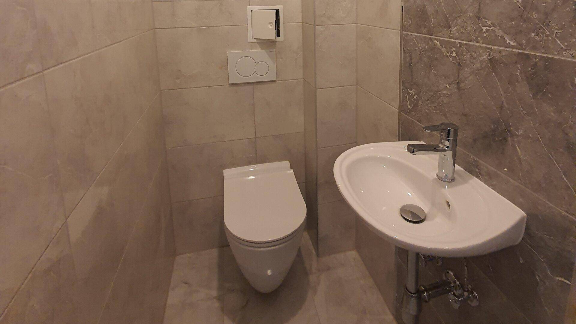 Modernes Gäste-WC mit Wand-WC, kleinem Waschbecken und Fliesen an Wänden und Boden.
