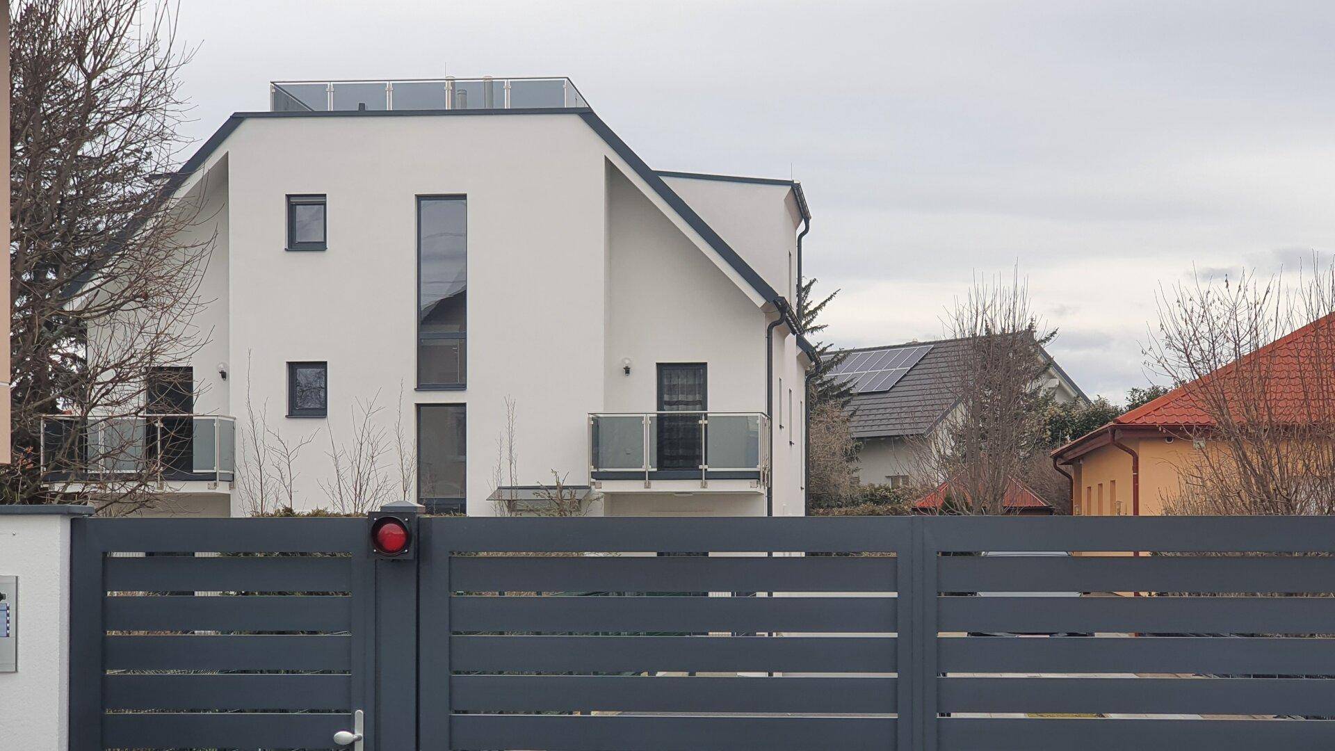 Moderne Wohnanlage mit weißer Fassade, Balkonen und einem Eingangstor.