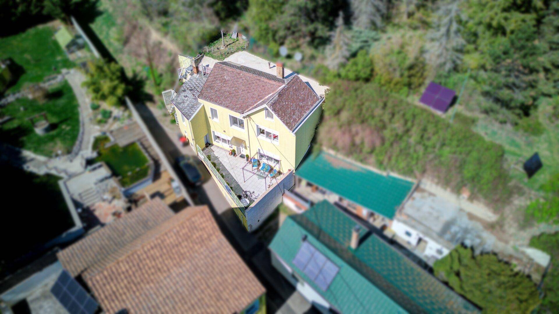 Vogelperspektive des gelben Wohnhauses mit Terrasse und Gartenbereich.