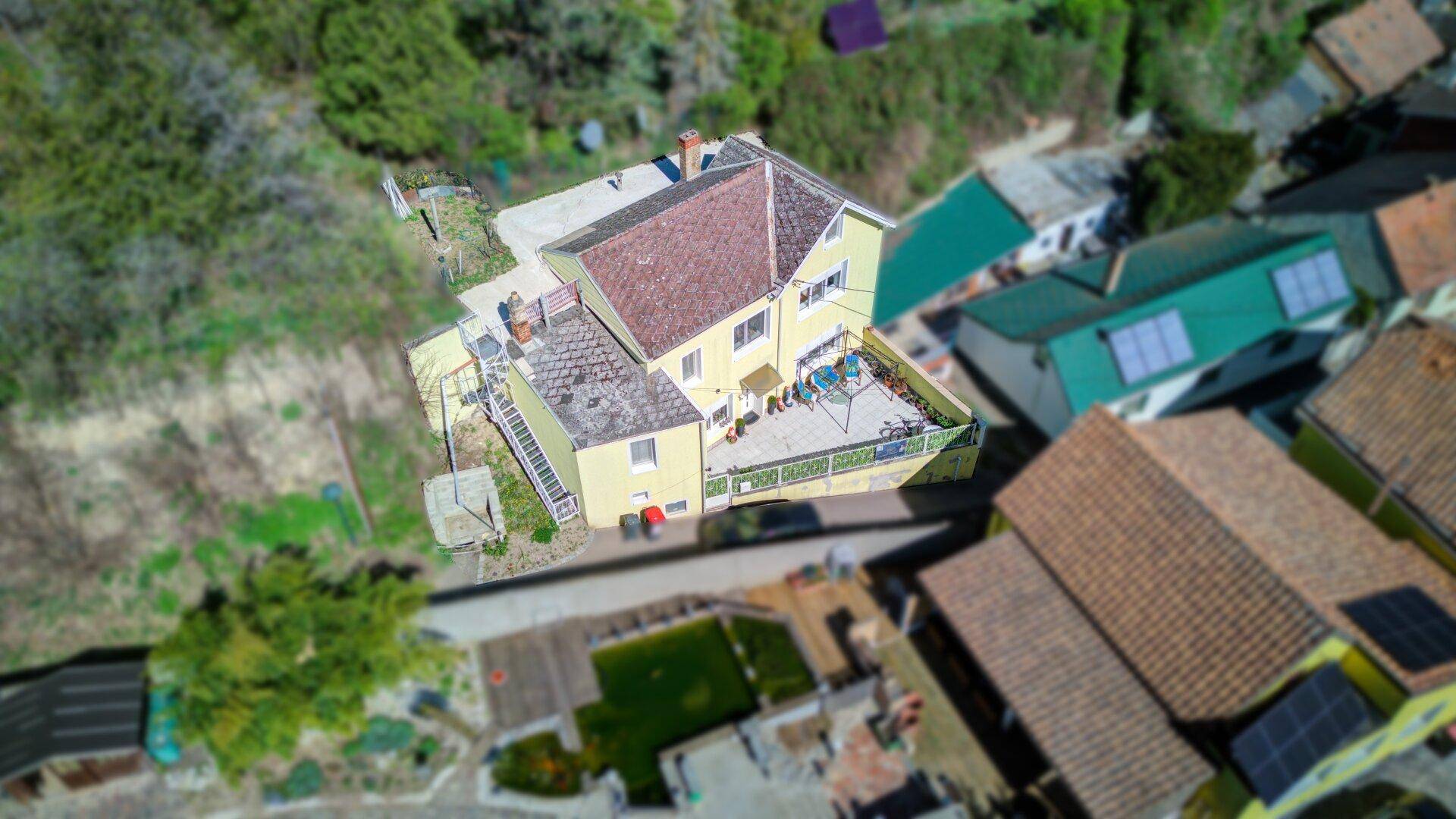Schrägansicht des gelben Hauses mit Terrasse und umgebender Natur.
