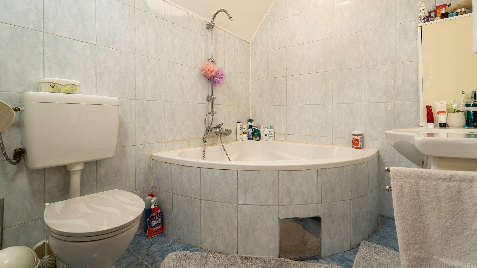 Gefliestes Badezimmer mit Eckbadewanne, Toilette und Waschbecken.