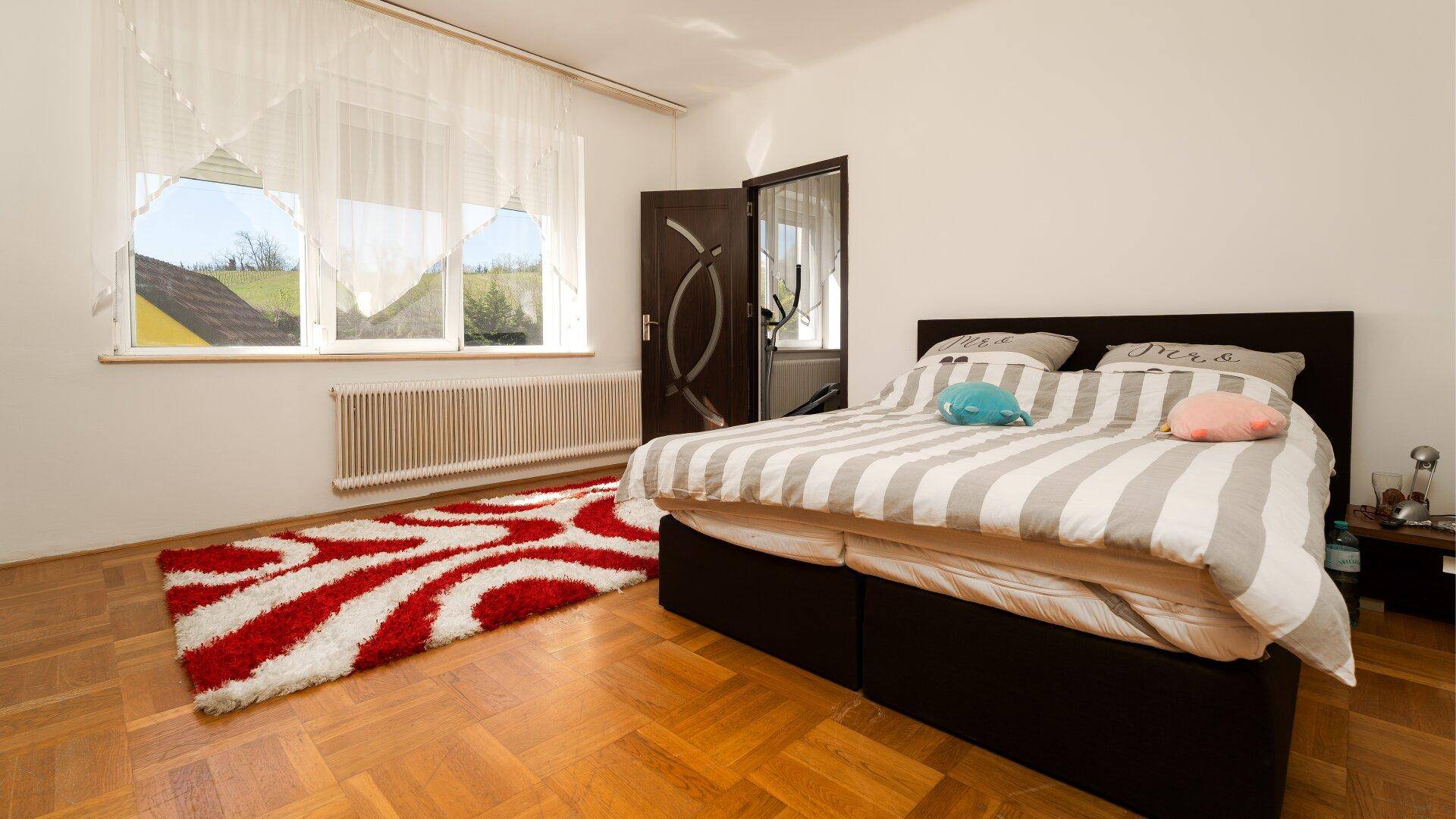 Helles Schlafzimmer mit Doppelbett, Parkettboden und großem Fenster.